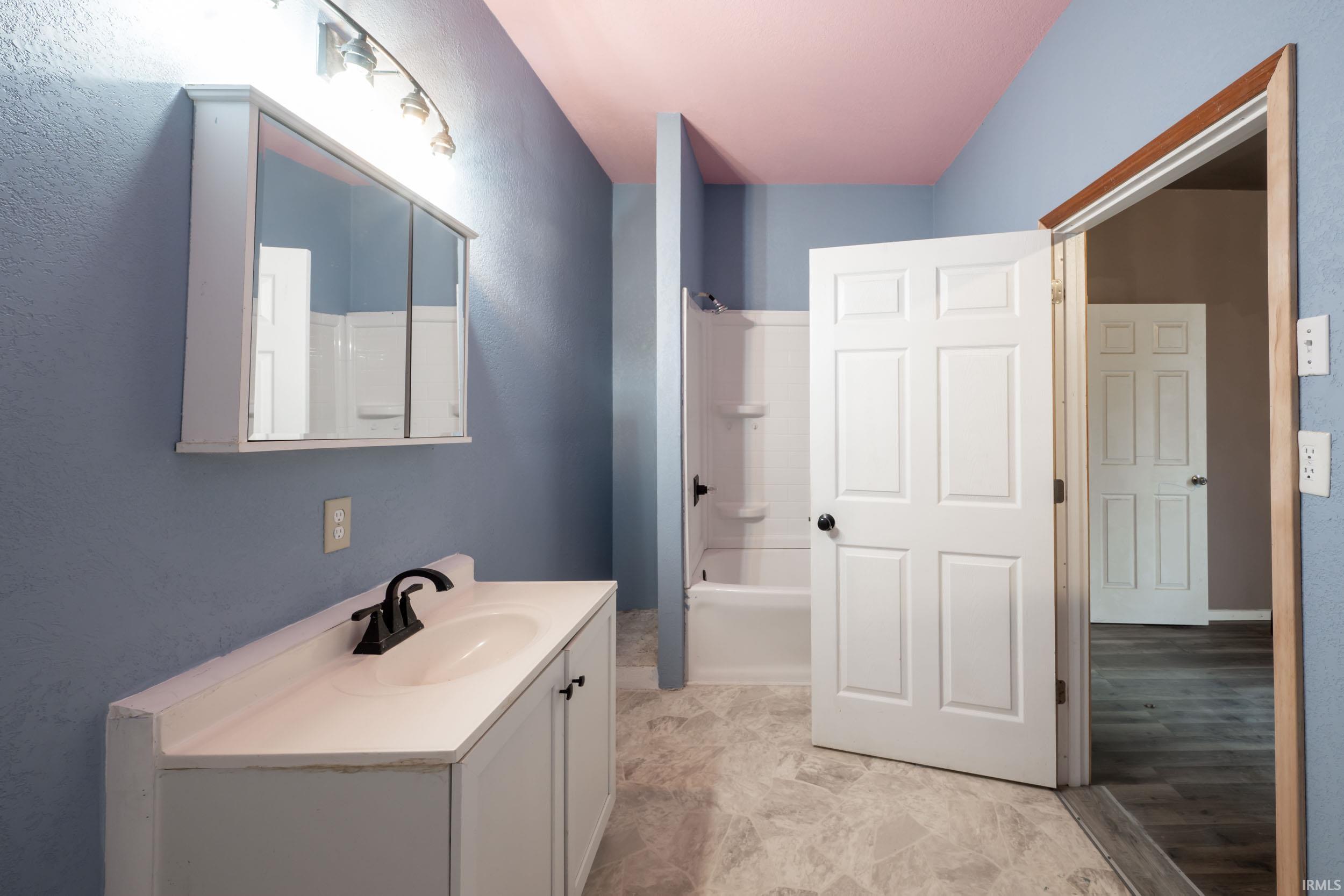 Full bath featuring tub / shower combination, vanity, and a textured wall