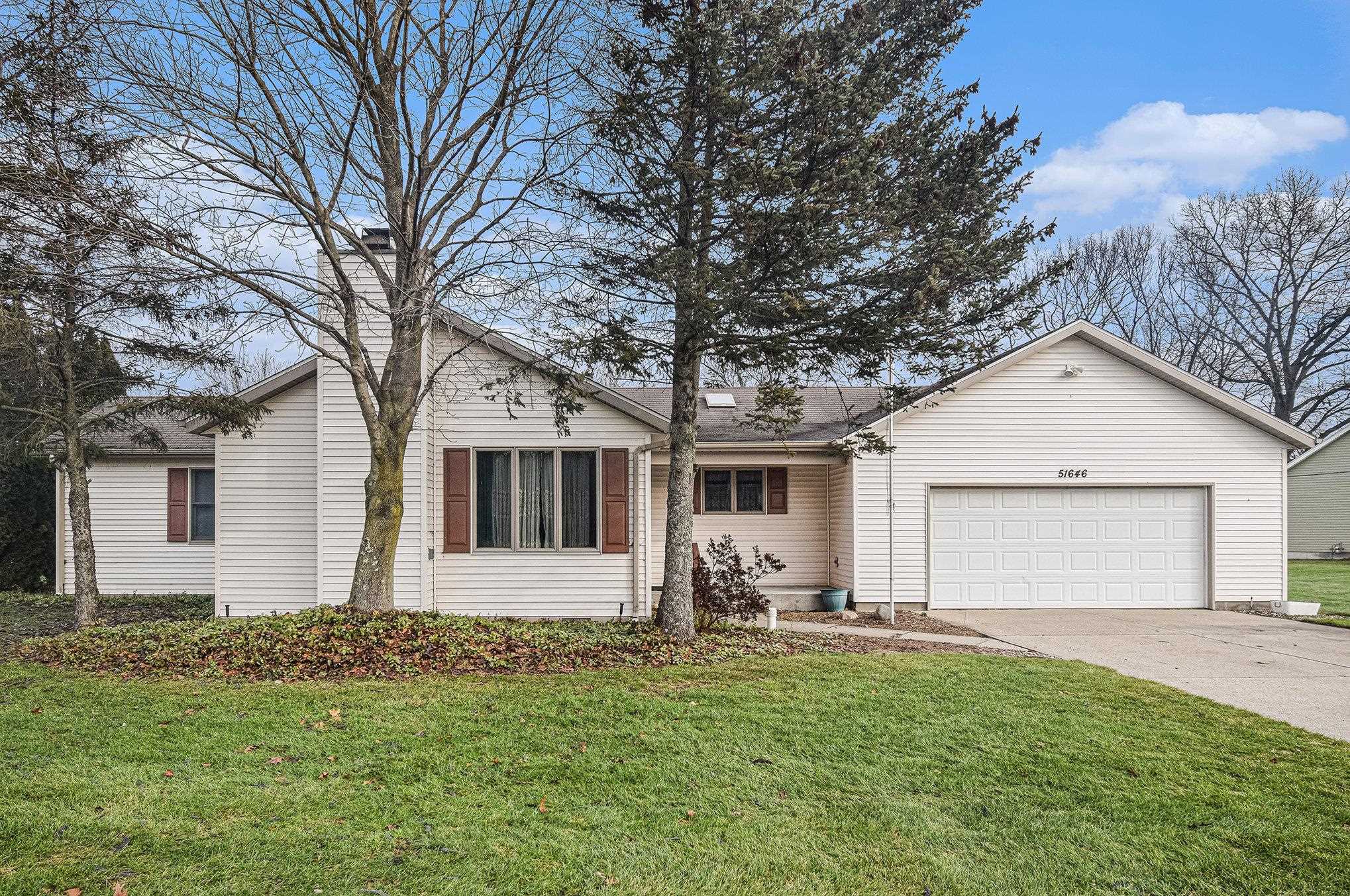 View of front of house featuring a yard, concrete driveway, a chimney, and a garage