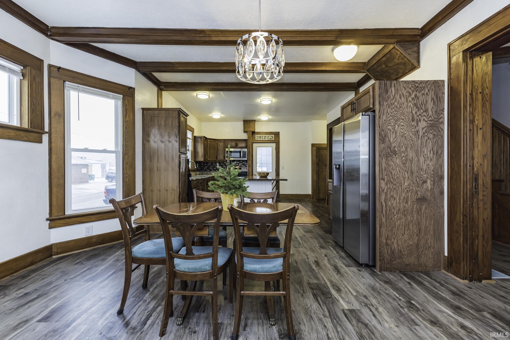 Dining area with healthy amount of natural light, beam ceiling, dark wood finished floors, and a chandelier