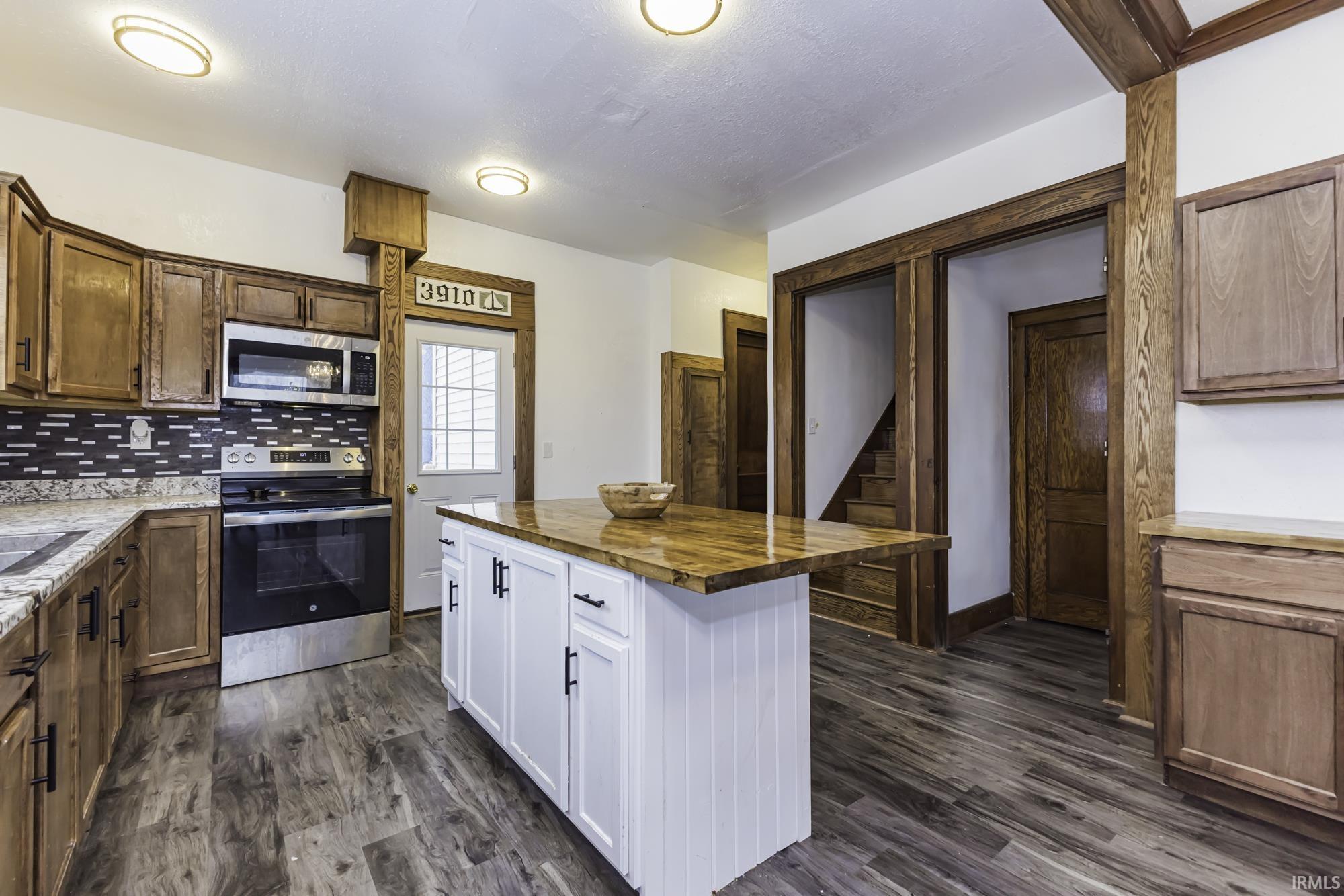 Kitchen with wooden counters, appliances with stainless steel finishes, a kitchen island, dark wood-type flooring, and backsplash