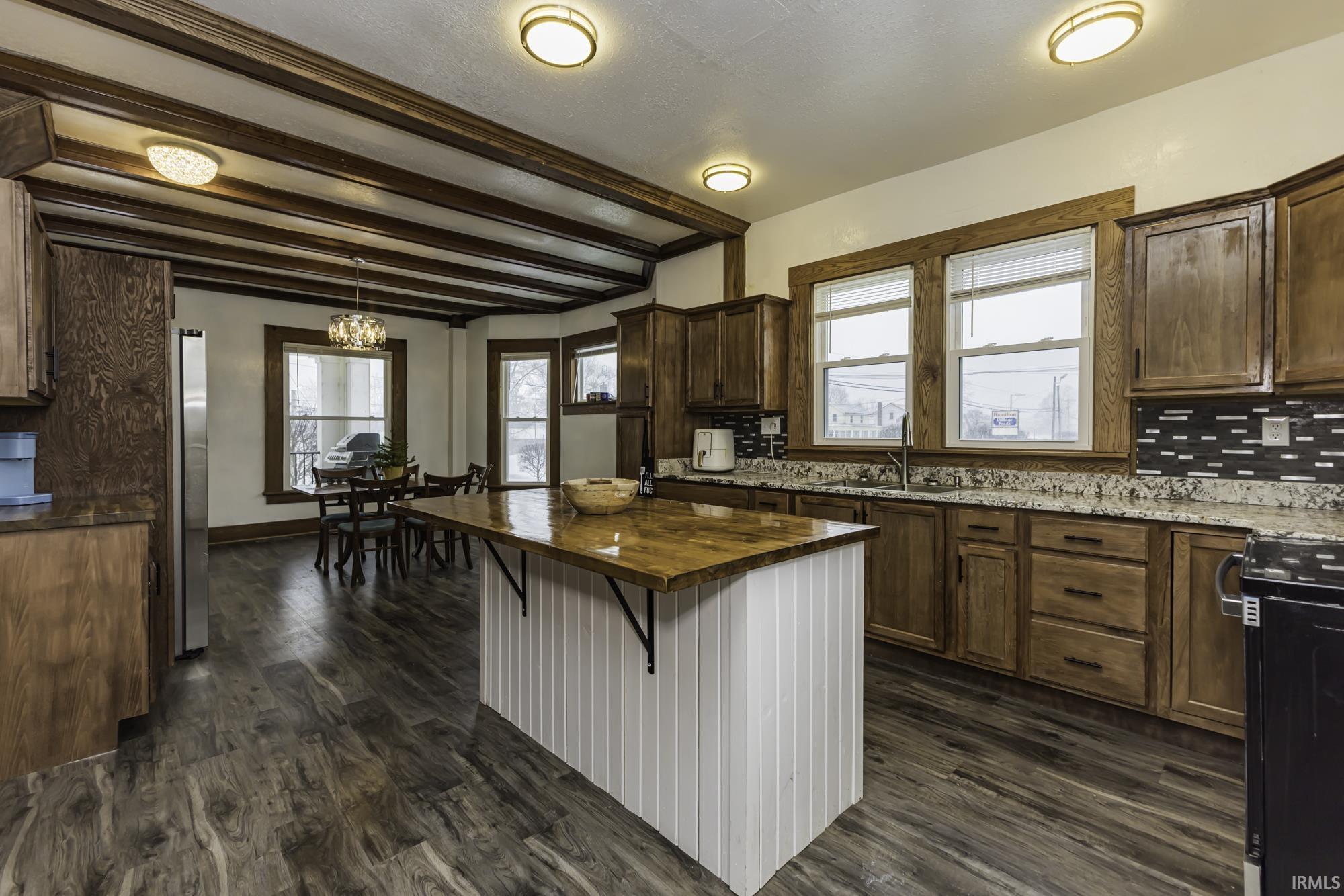 Kitchen with decorative backsplash, butcher block countertops, healthy amount of natural light, hanging light fixtures, and beam ceiling