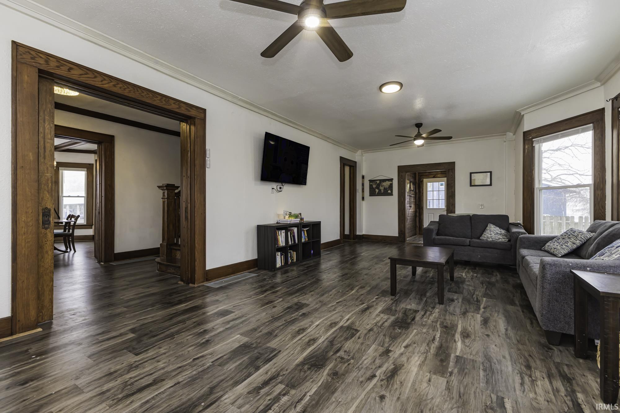Living room featuring plenty of natural light, dark wood-style floors, crown molding, and a ceiling fan