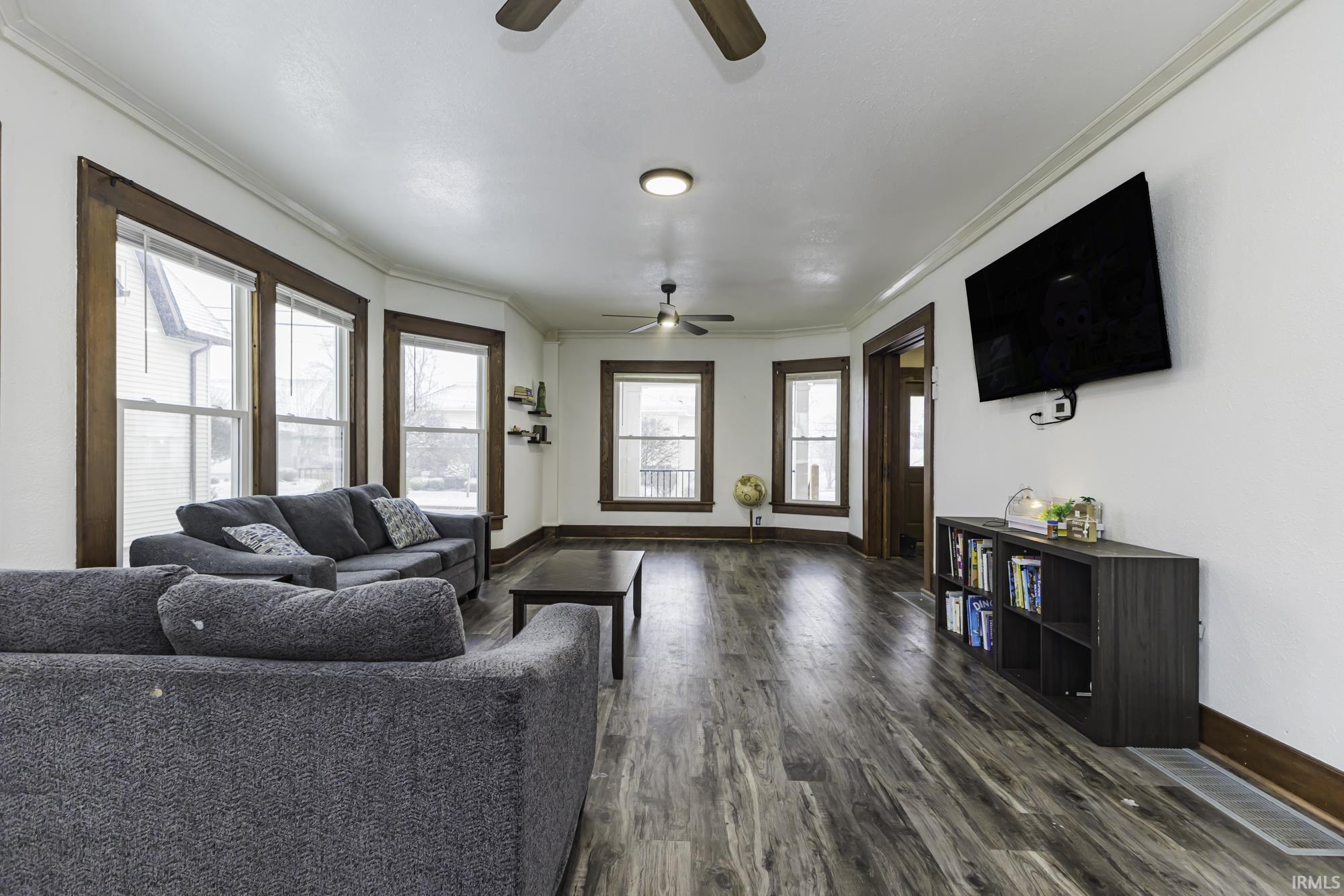 Living room featuring ceiling fan, crown molding, and dark wood-type flooring
