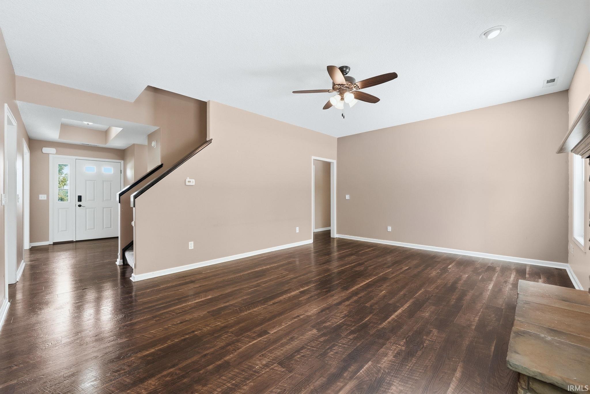 Spacious living area featuring rich wood-finish flooring, a ceiling fan, and neutral wall tones