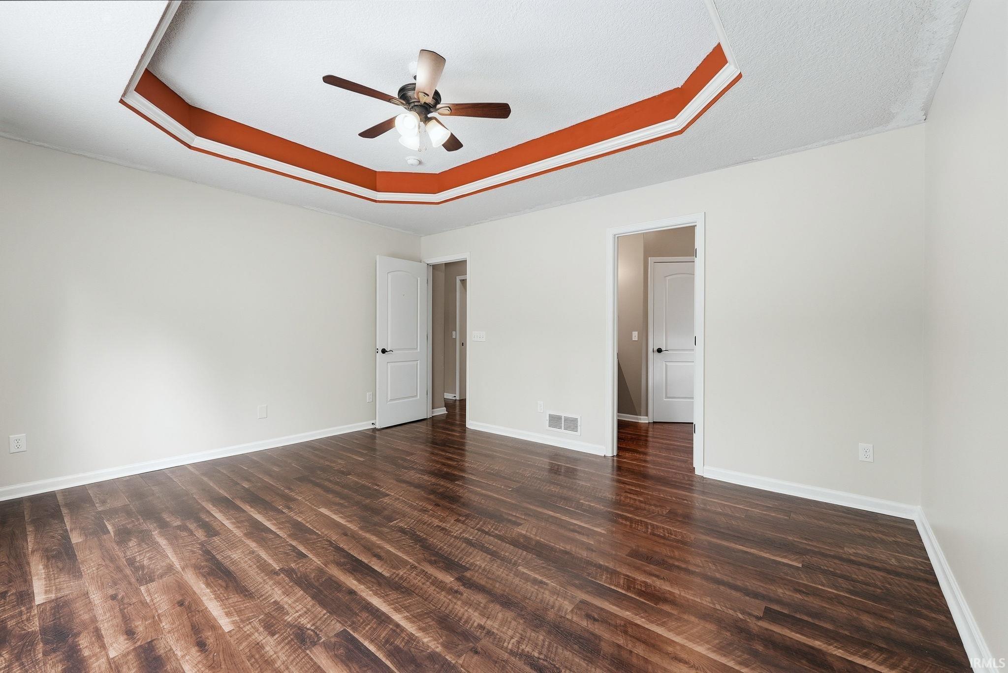 Spacious room featuring wood-finish flooring, a tray ceiling with accent trim, and a ceiling fan