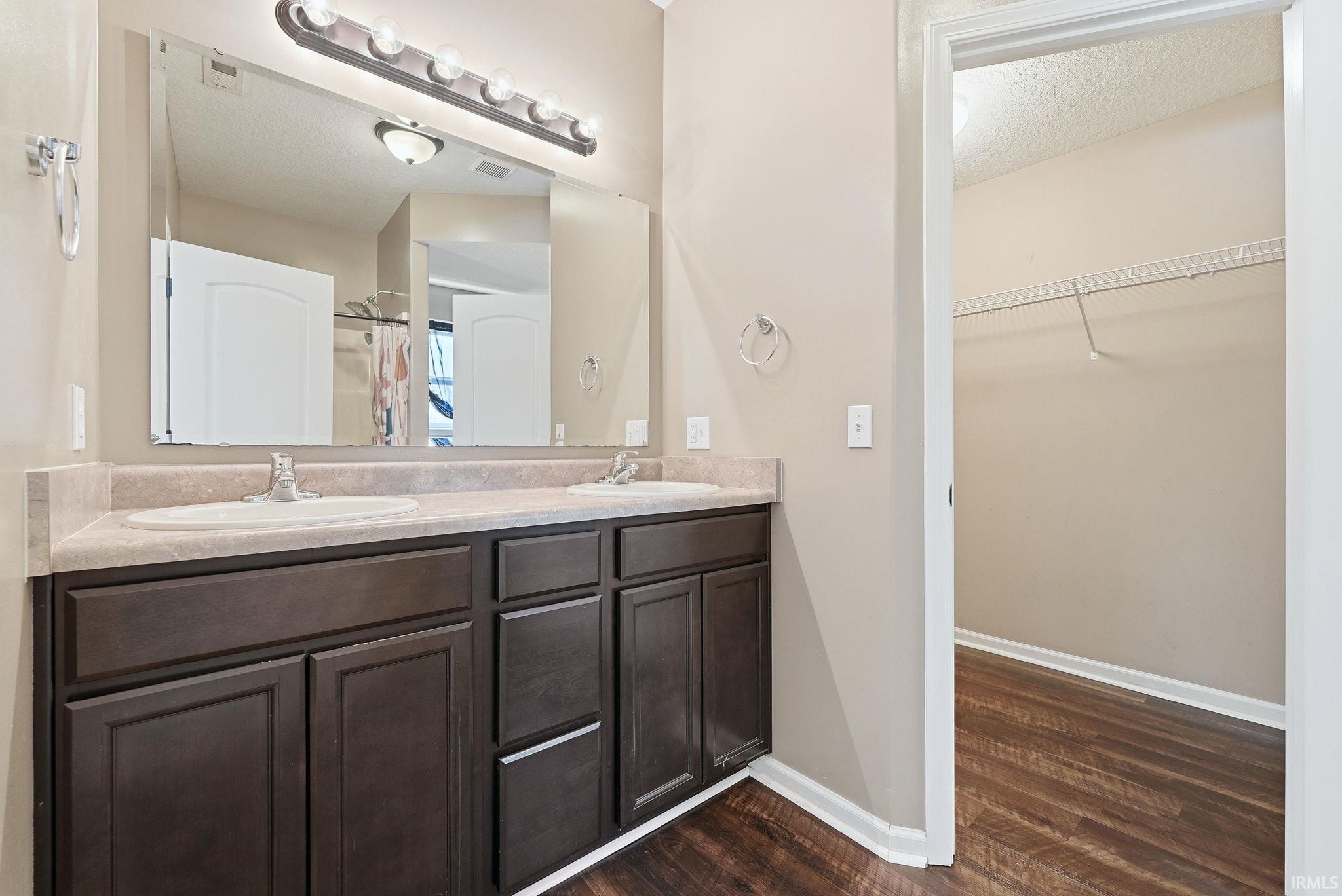 Dual sink vanity featuring dark wood-finish cabinetry, a neutral countertop, and a large wall-mounted mirror