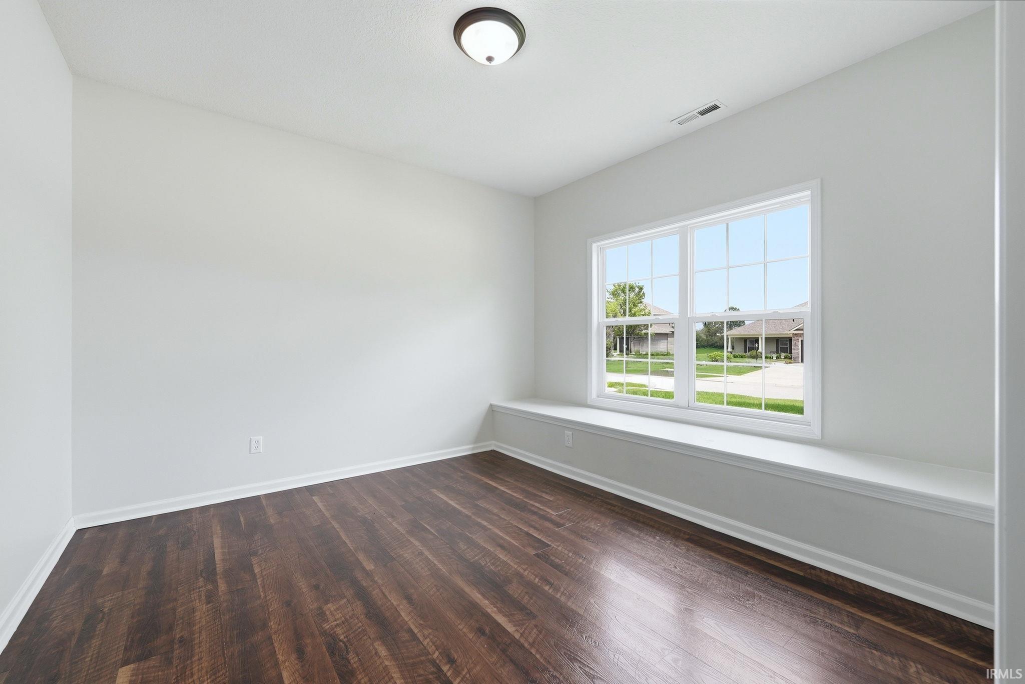 Bright interior space featuring a large window with white muntins, a built-in window seat, wood-finish flooring, white baseboards, and a flush-mount ceiling light fixture