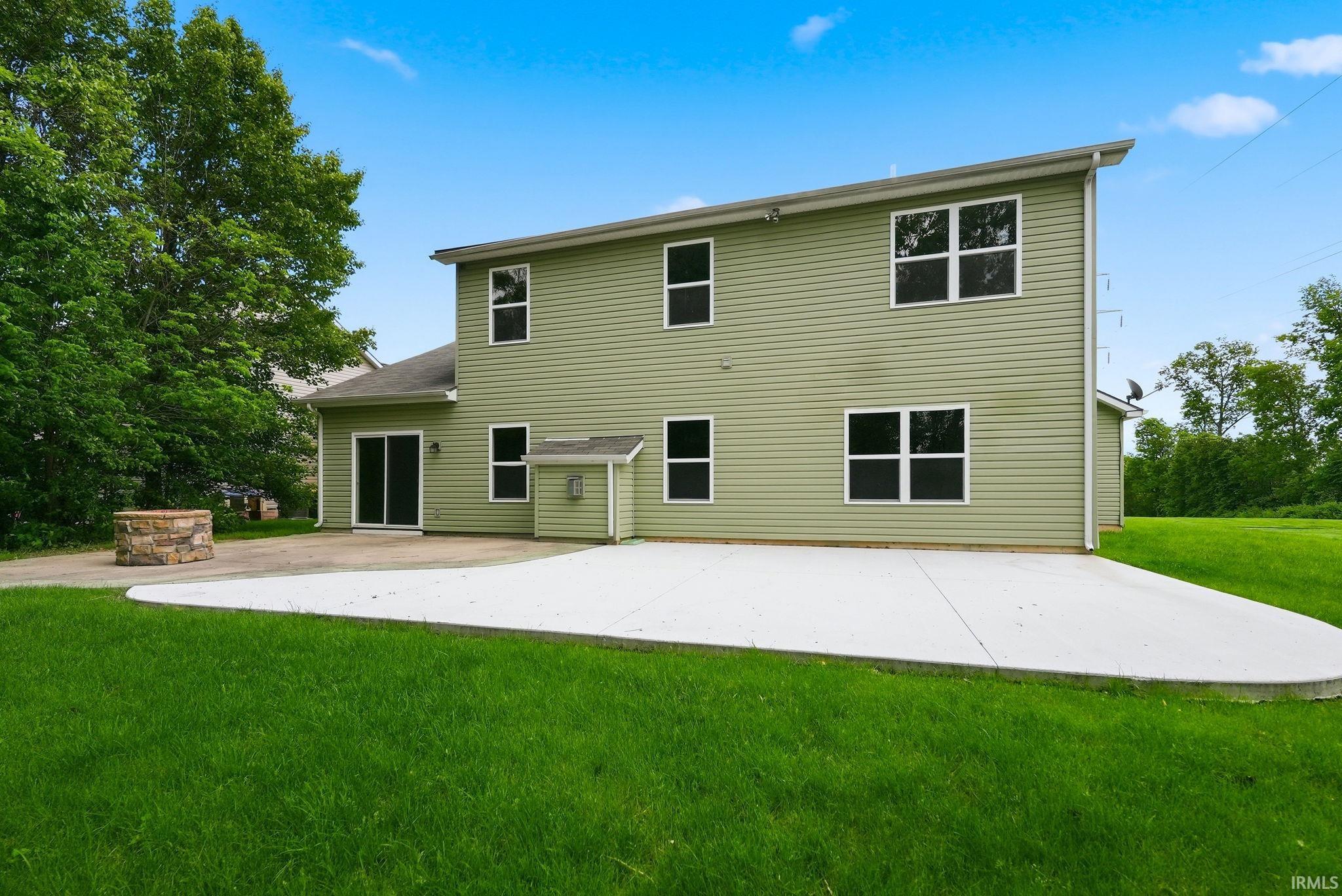 Rear exterior featuring a spacious concrete patio, a stone fire pit, and sliding glass doors