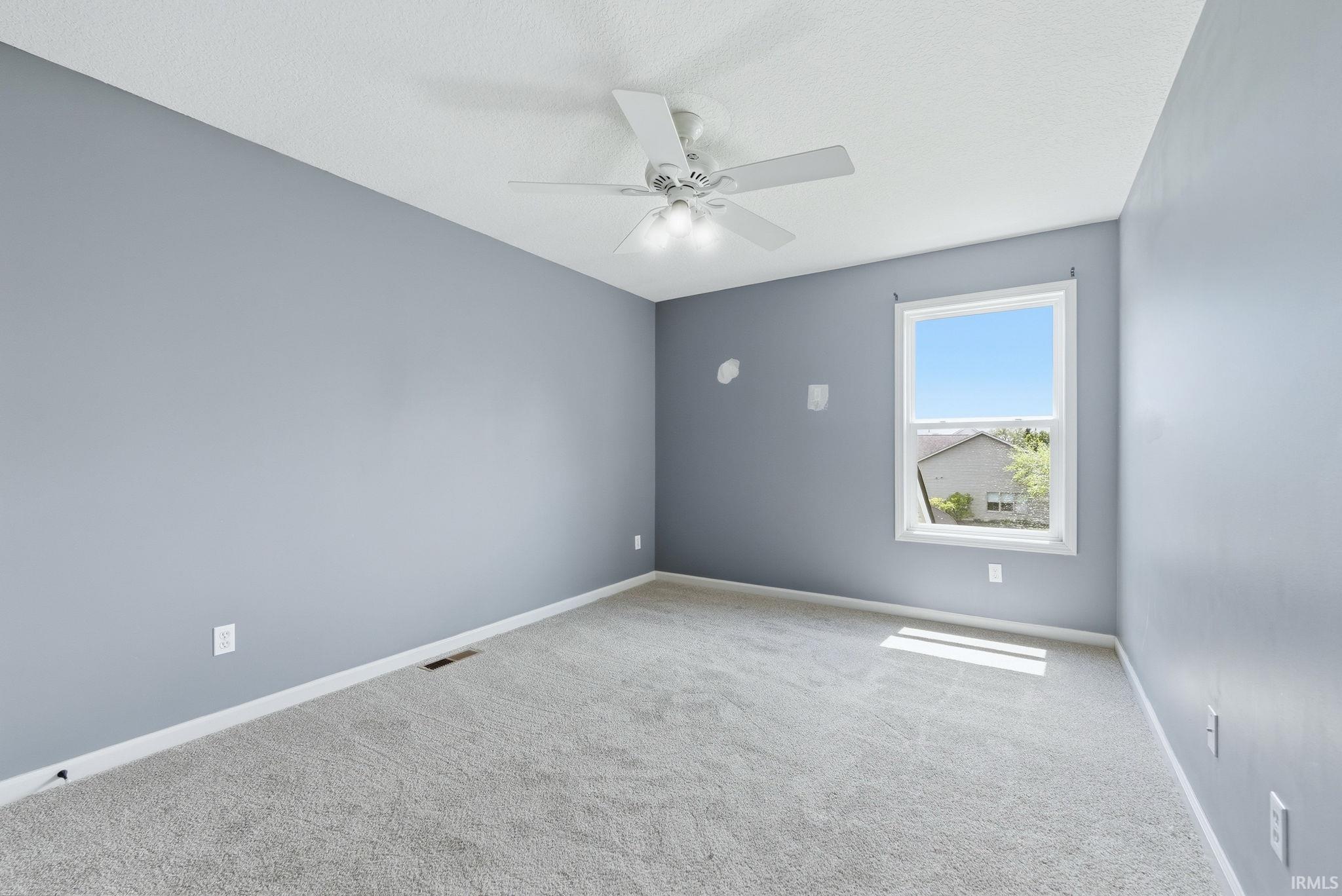 Spacious room featuring light gray carpeting and a white ceiling fan with integrated lighting