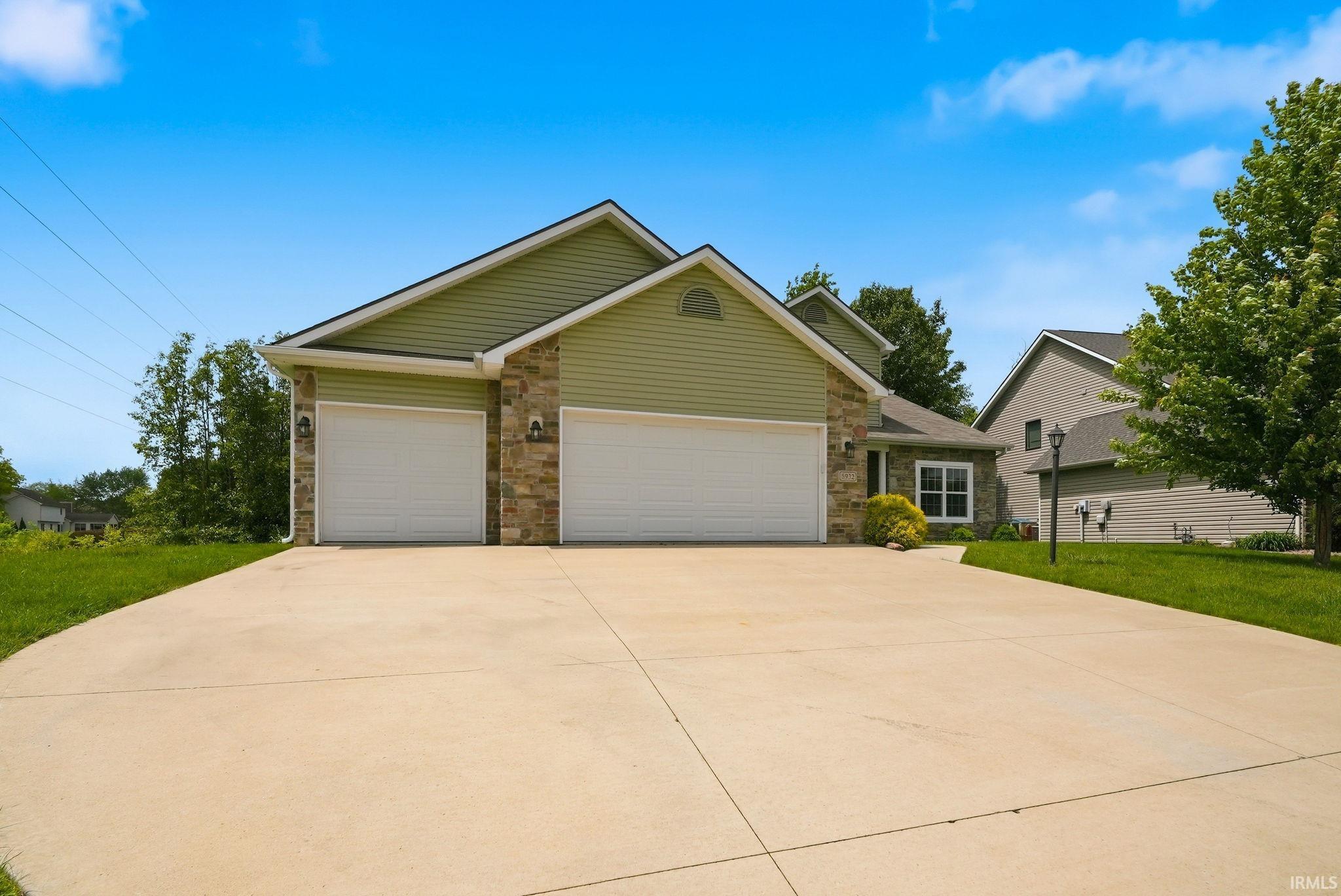 Exterior featuring green siding, stone accents, a two-car garage, and a concrete driveway