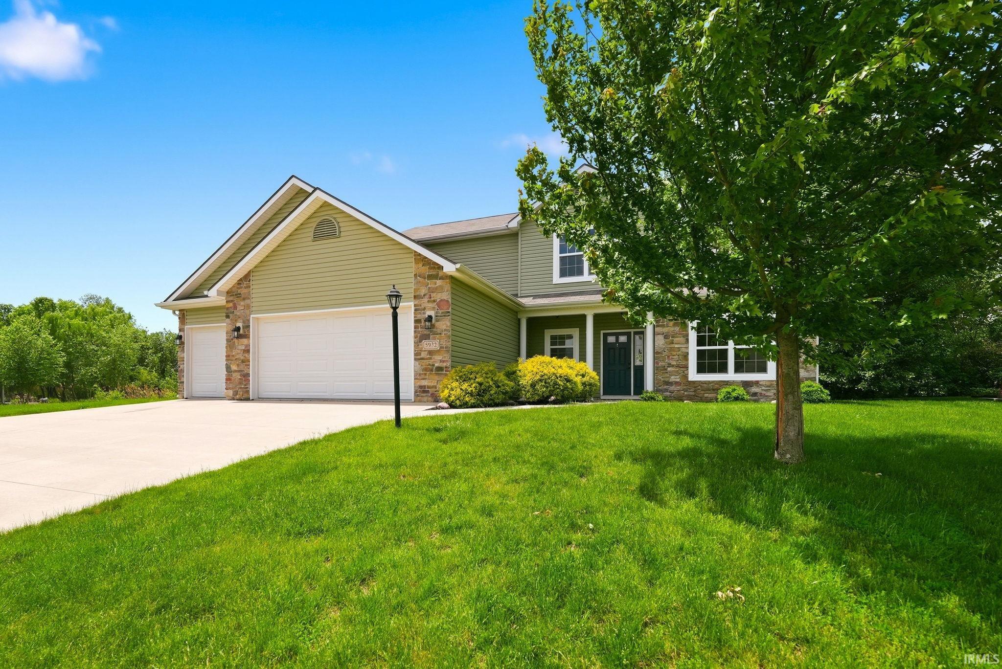 Contemporary residence featuring a two-story design, a two-car garage, and a light green siding exterior with stone accents