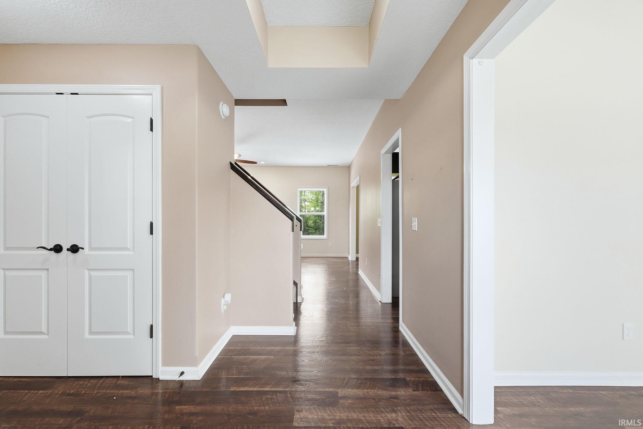 Hallway featuring wood-finish flooring, light tan walls, white trim, and a prominent staircase with dark railings
