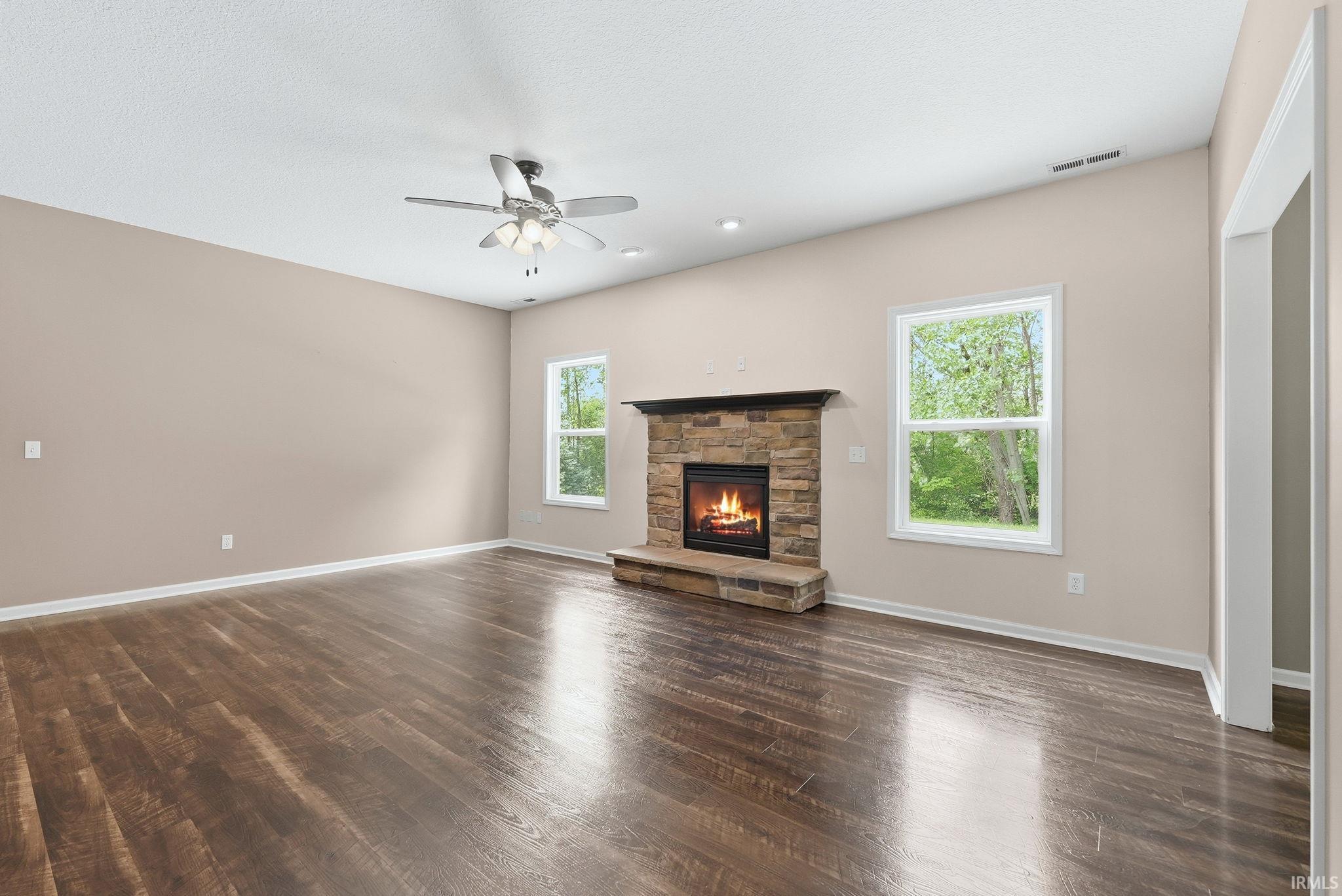 Spacious room featuring a stone-clad fireplace with a wood mantel, wood-finish flooring, and white trim