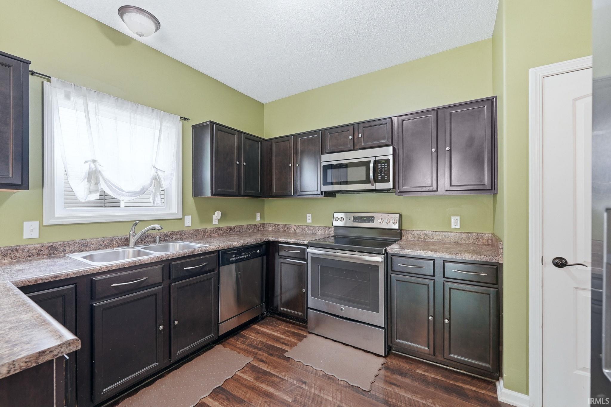 Kitchen featuring dark wood-finish cabinetry with stainless steel hardware, a dual basin stainless steel sink, stainless steel appliances, and wood-finish flooring