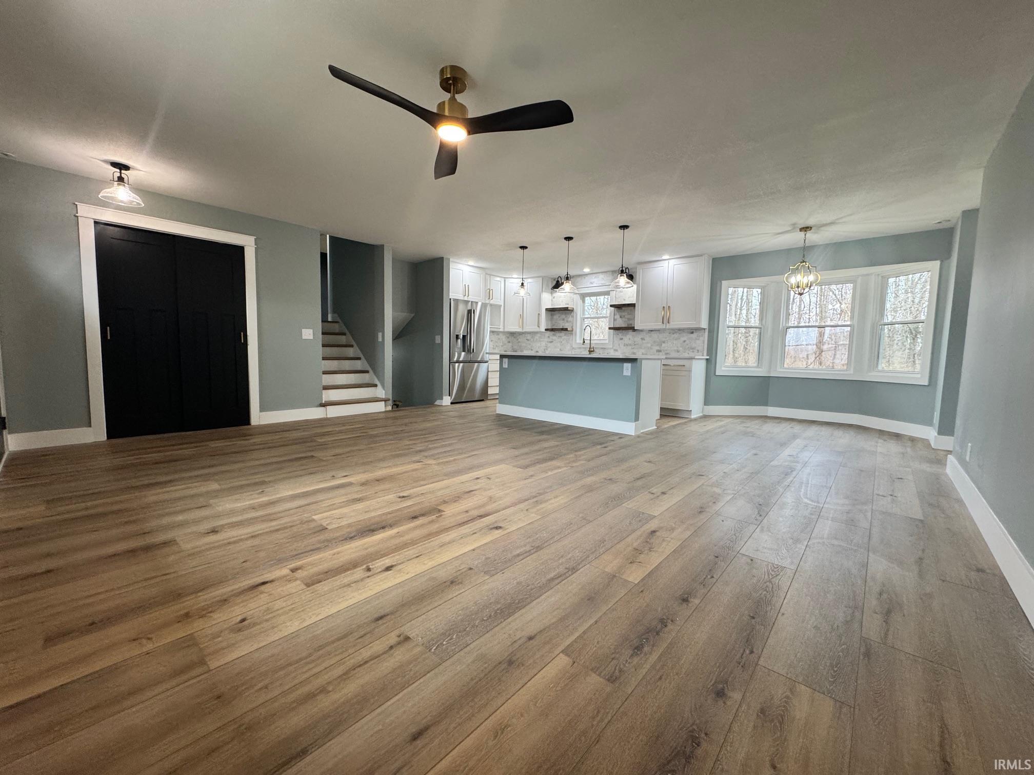 Unfurnished living room with stairway, a ceiling fan, a chandelier, and light wood-style flooring