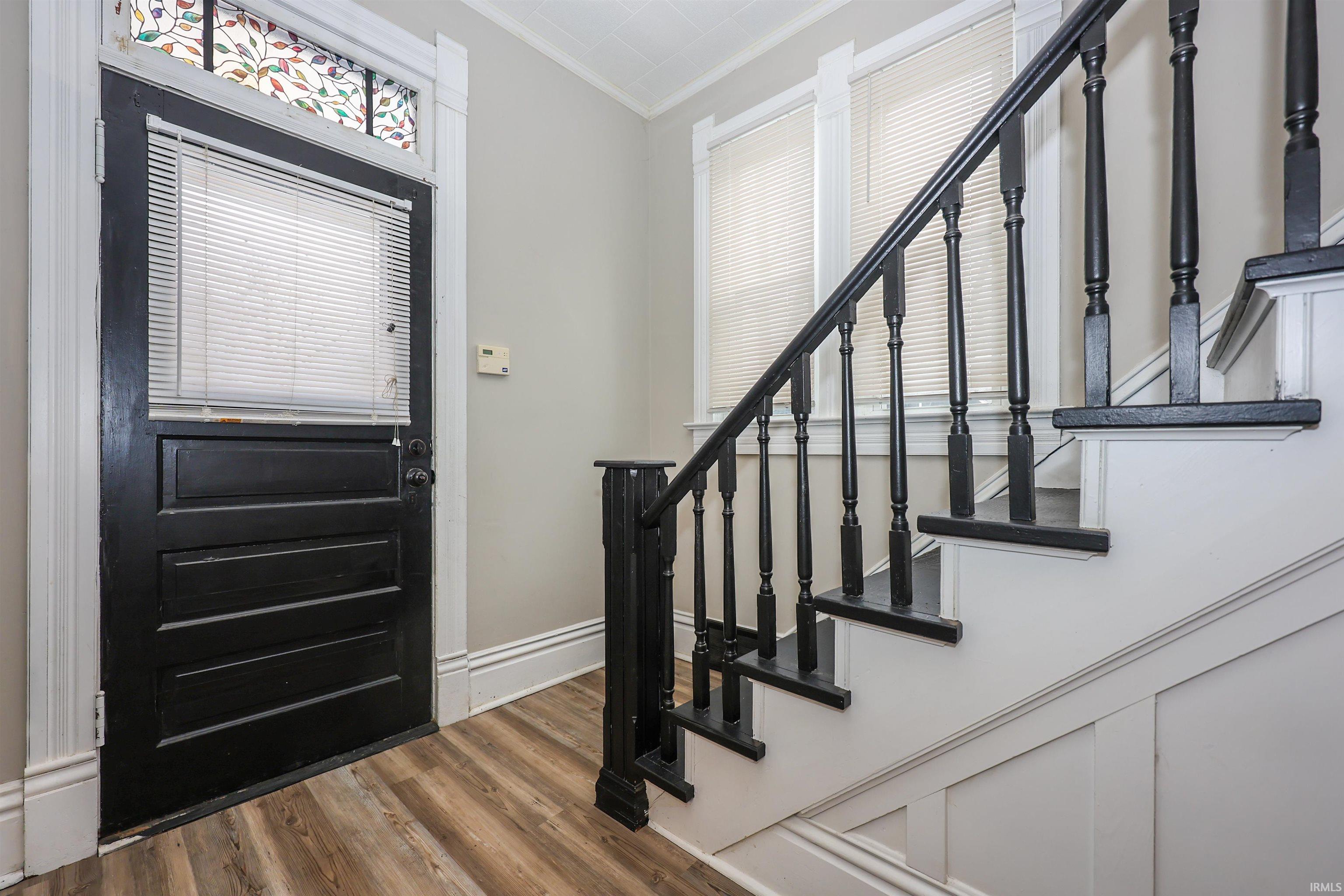 Foyer with ornamental molding, stairs, and dark wood finished floors