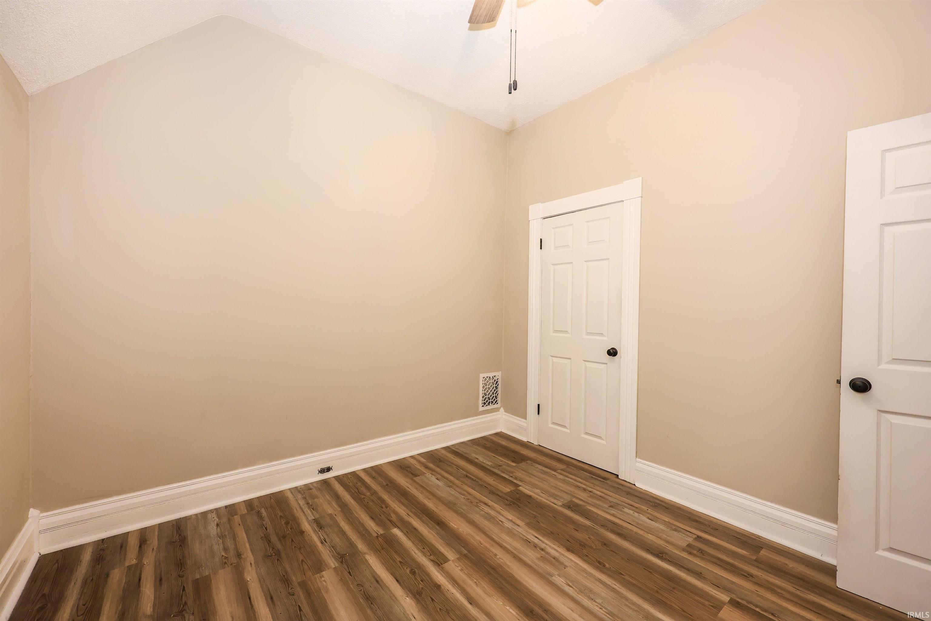 Empty room featuring dark wood-type flooring, ceiling fan, and lofted ceiling