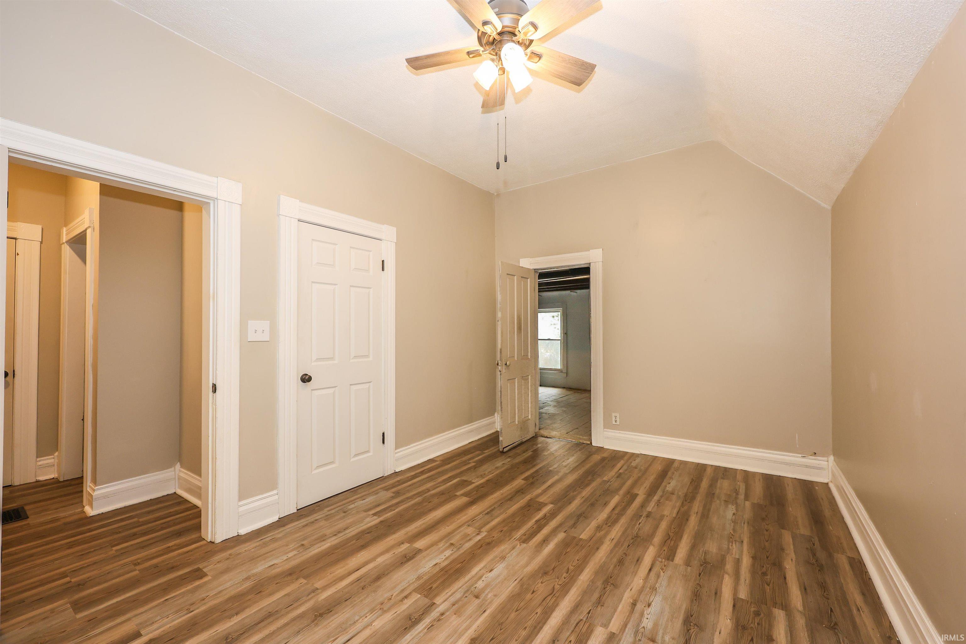 Unfurnished bedroom featuring wood finished floors, ceiling fan, and lofted ceiling