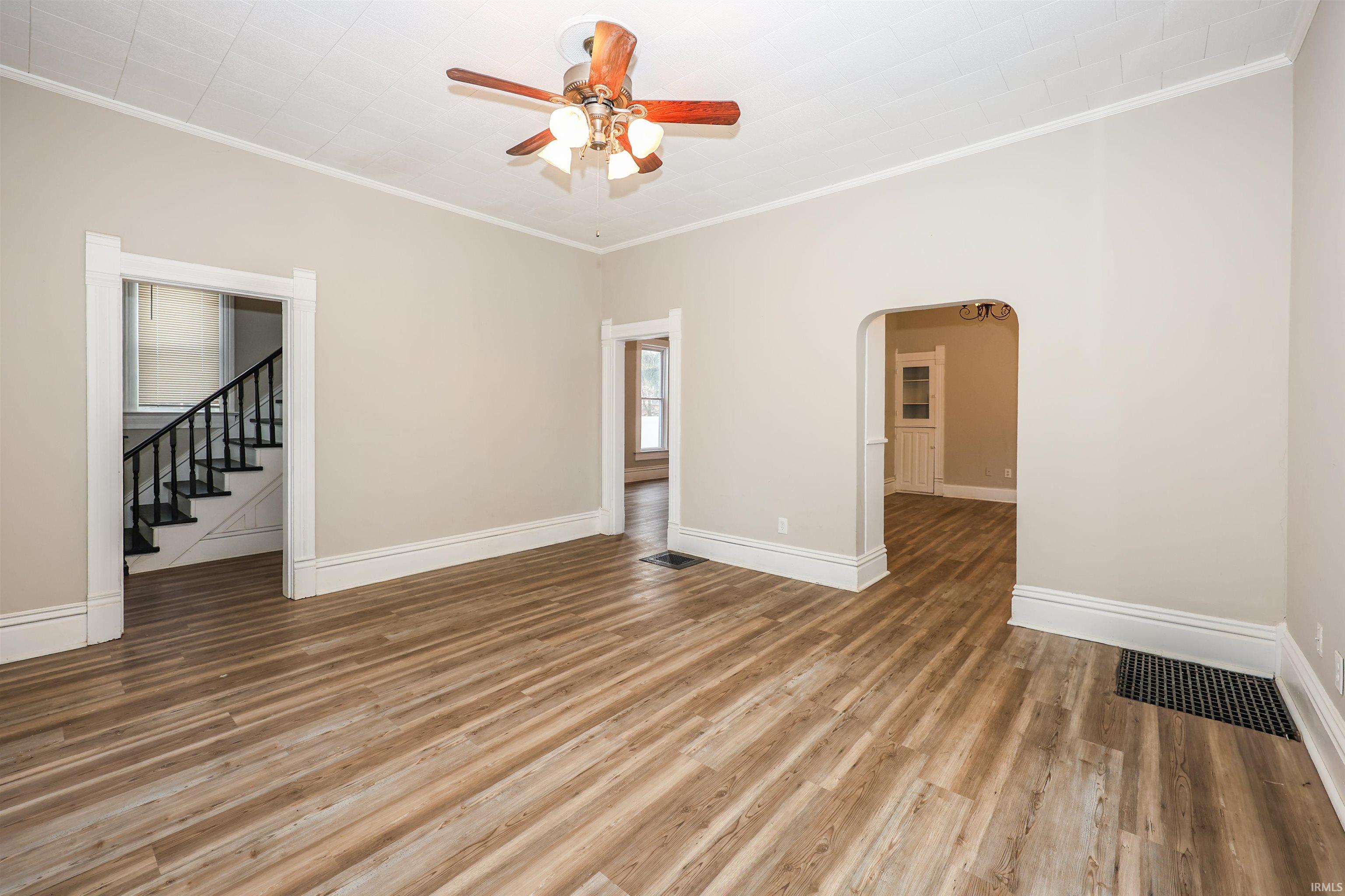Spare room with arched walkways, light wood finished floors, stairs, crown molding, and a ceiling fan
