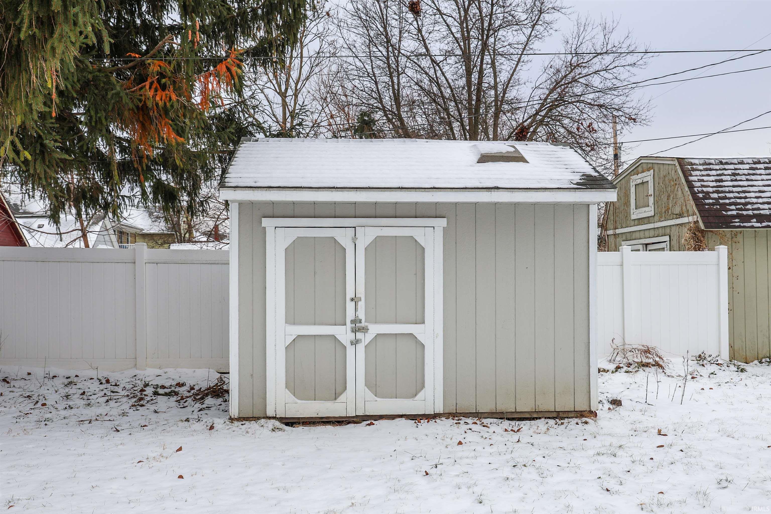 Snow covered structure with a fenced backyard and a storage shed