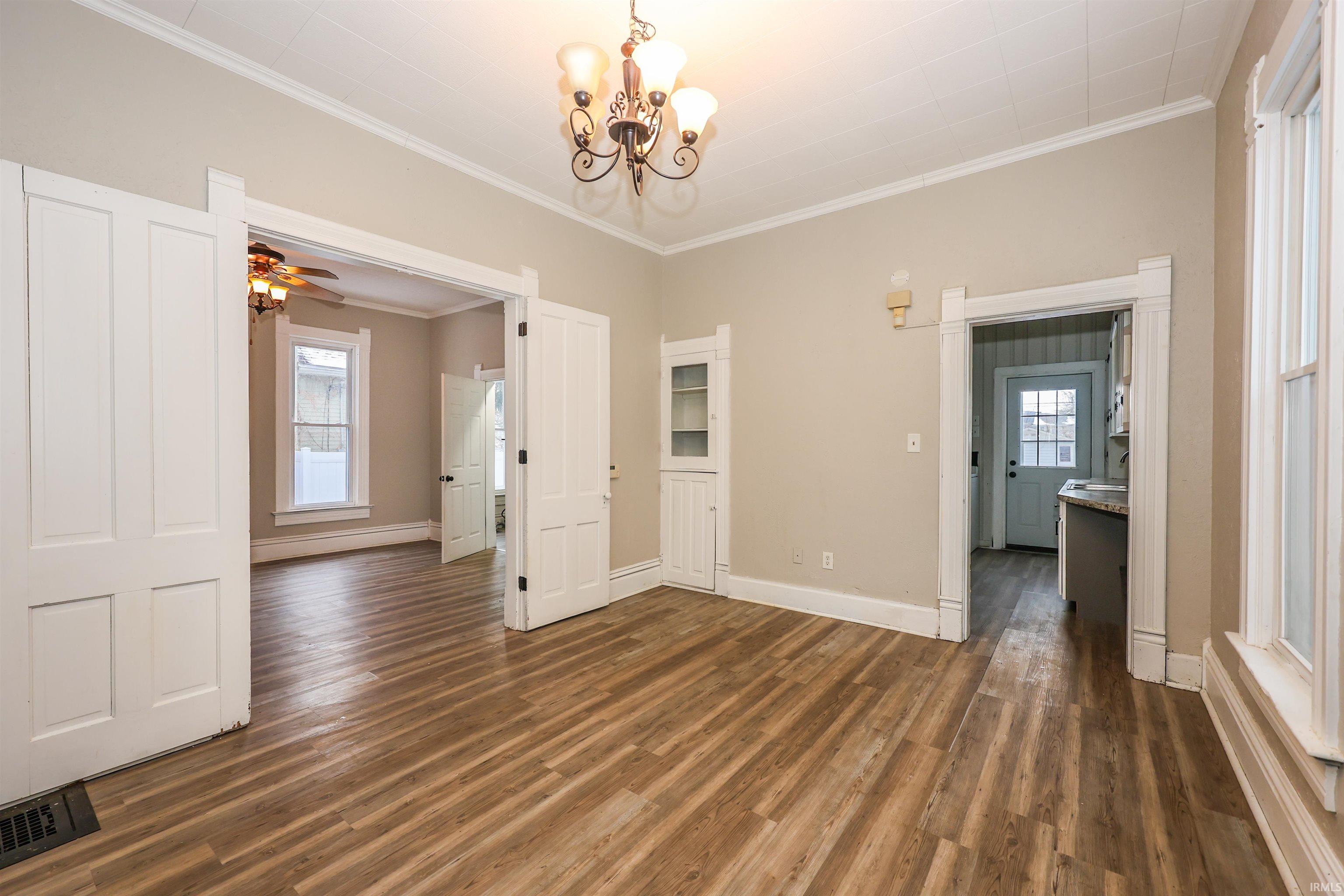 Unfurnished dining area featuring crown molding, dark wood-style flooring, a chandelier, plenty of natural light, and a ceiling fan