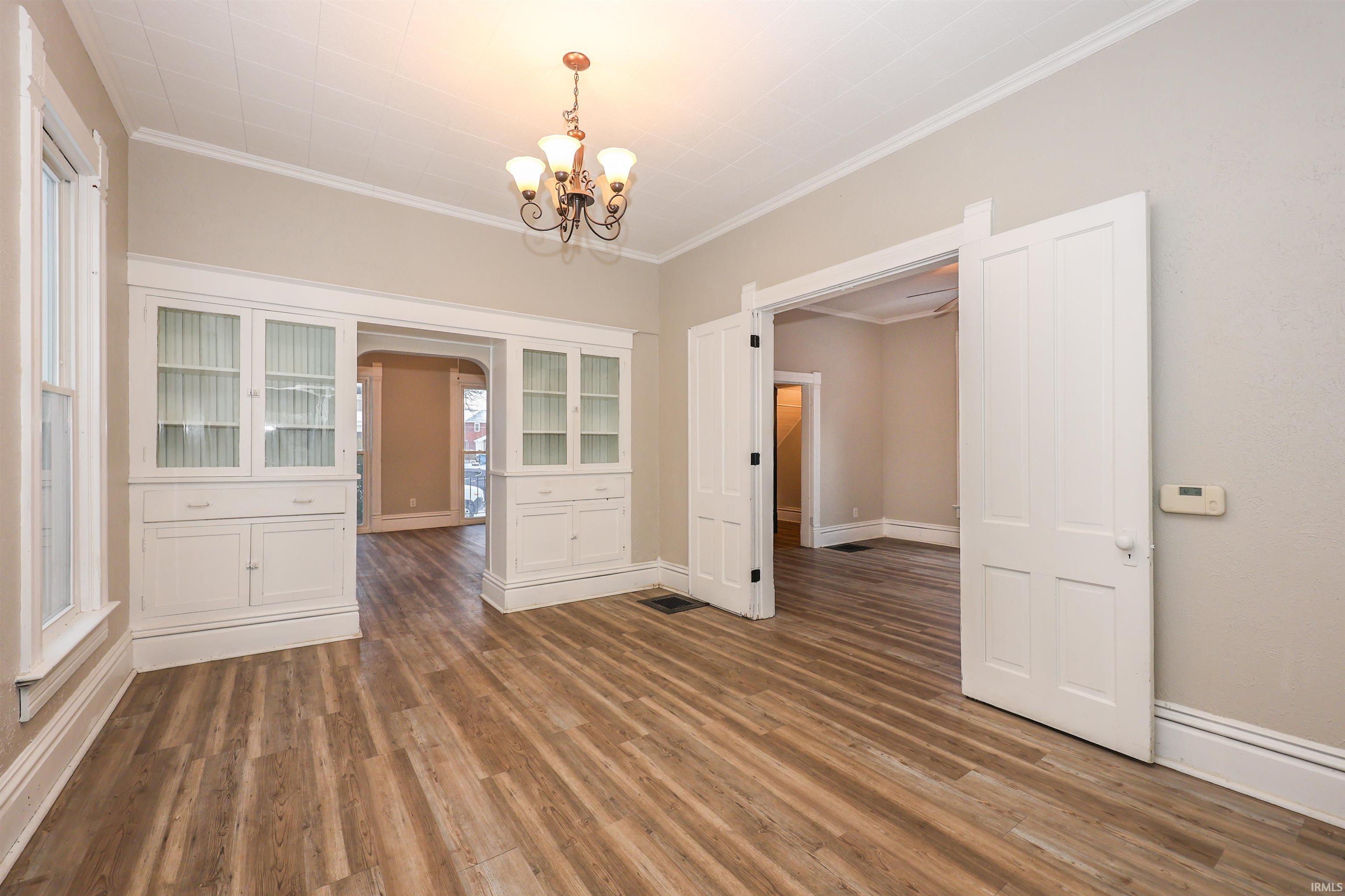 Unfurnished dining area featuring dark wood-style flooring, ornamental molding, a chandelier, and arched walkways
