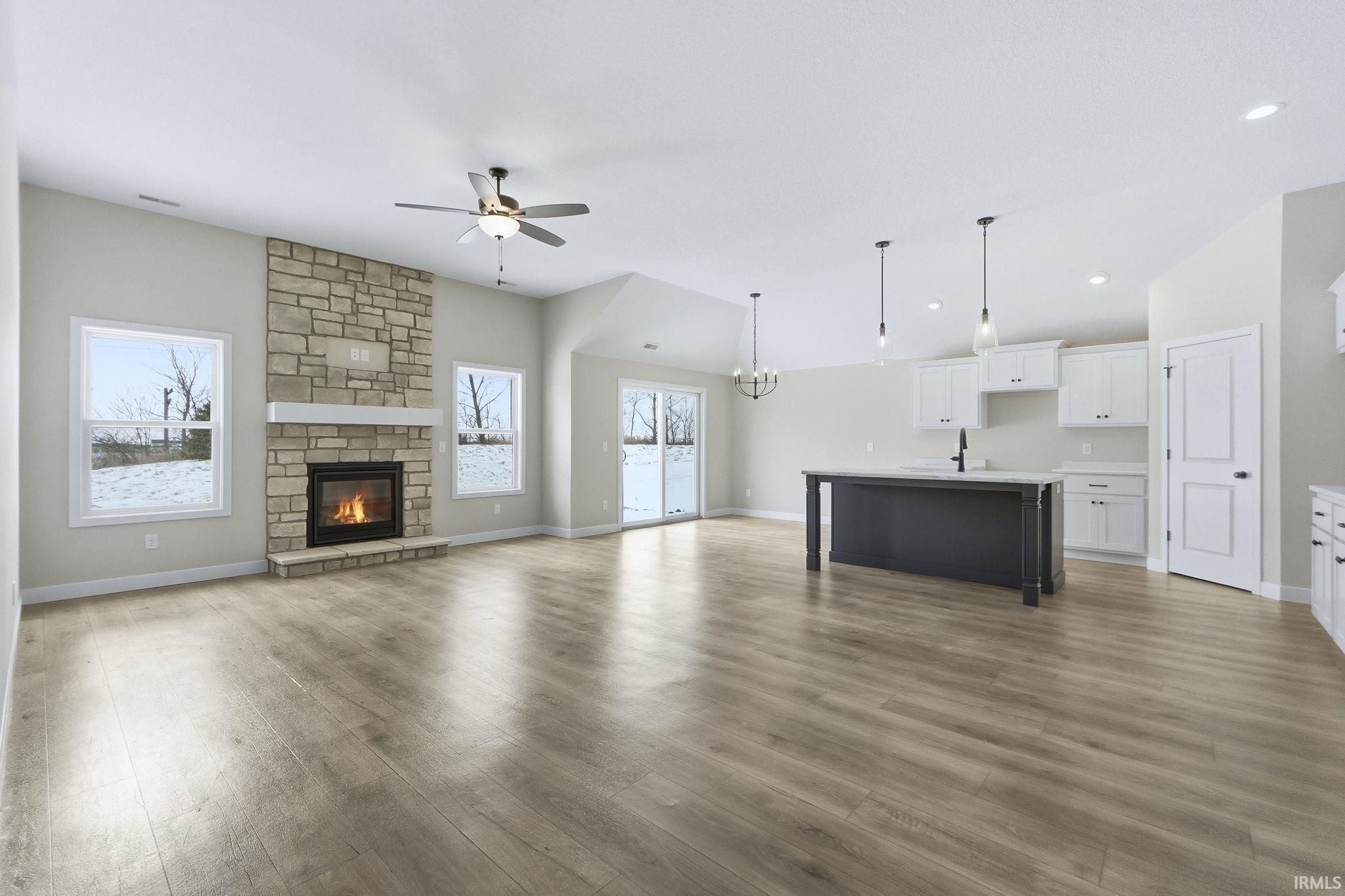 Unfurnished living room with a fireplace, a ceiling fan, a chandelier, and wood finished floors