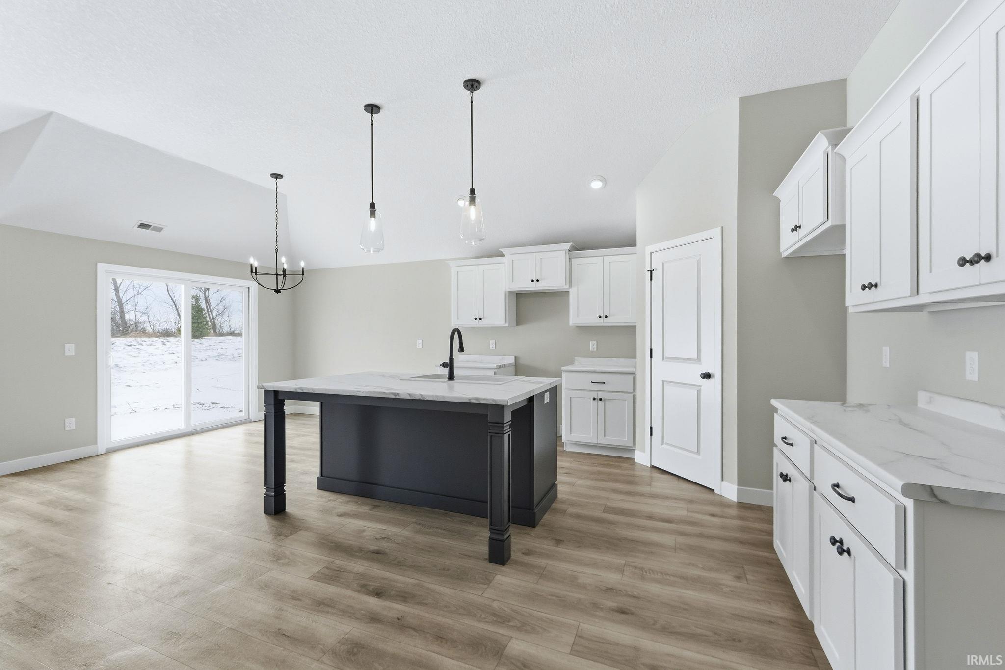 Kitchen featuring white cabinets, a kitchen island with sink, a breakfast bar, pendant lighting, and lofted ceiling