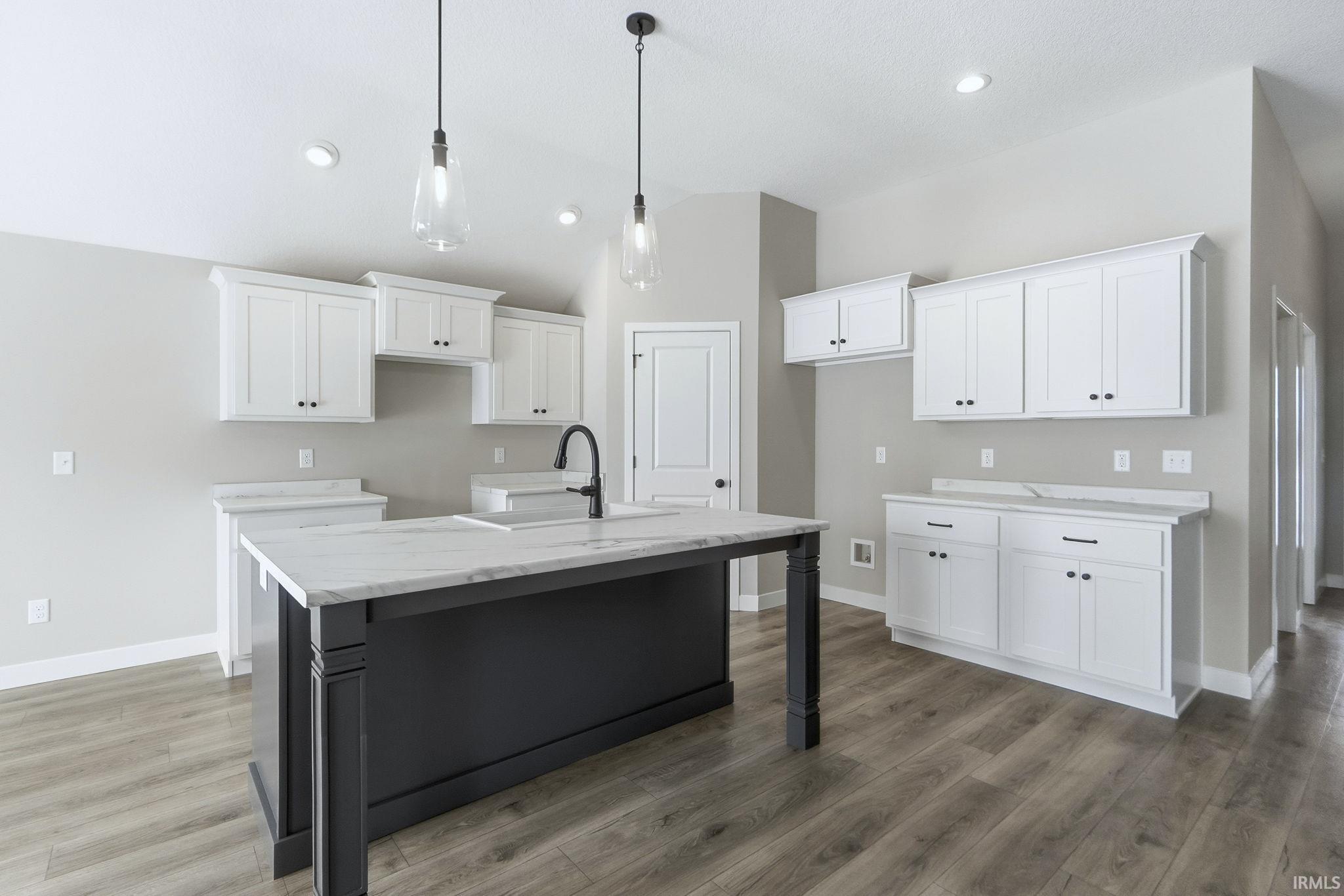 Kitchen with white cabinets, hanging light fixtures, a center island with sink, vaulted ceiling, and a kitchen breakfast bar