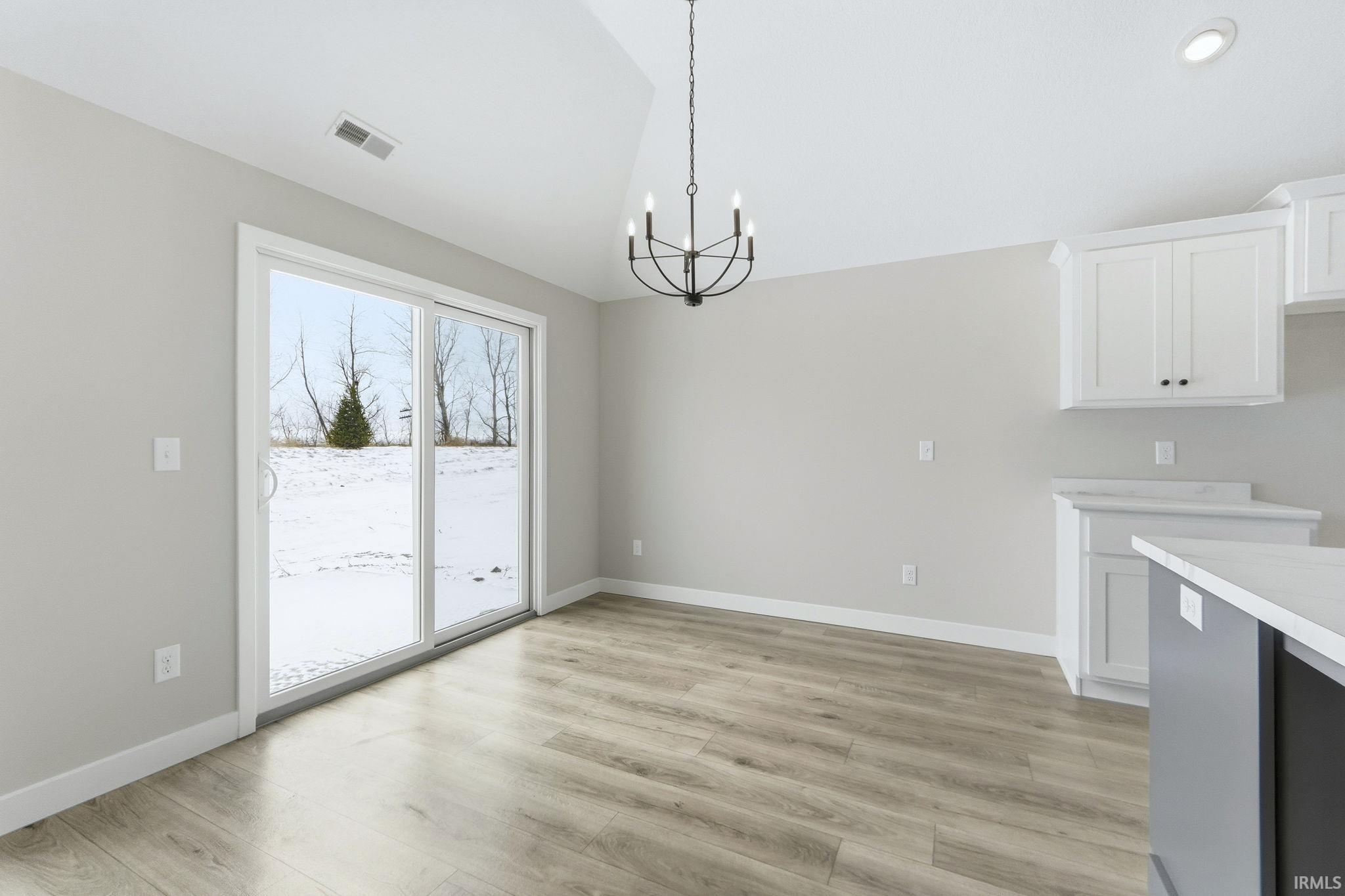 Unfurnished dining area with lofted ceiling, a chandelier, and light wood finished floors