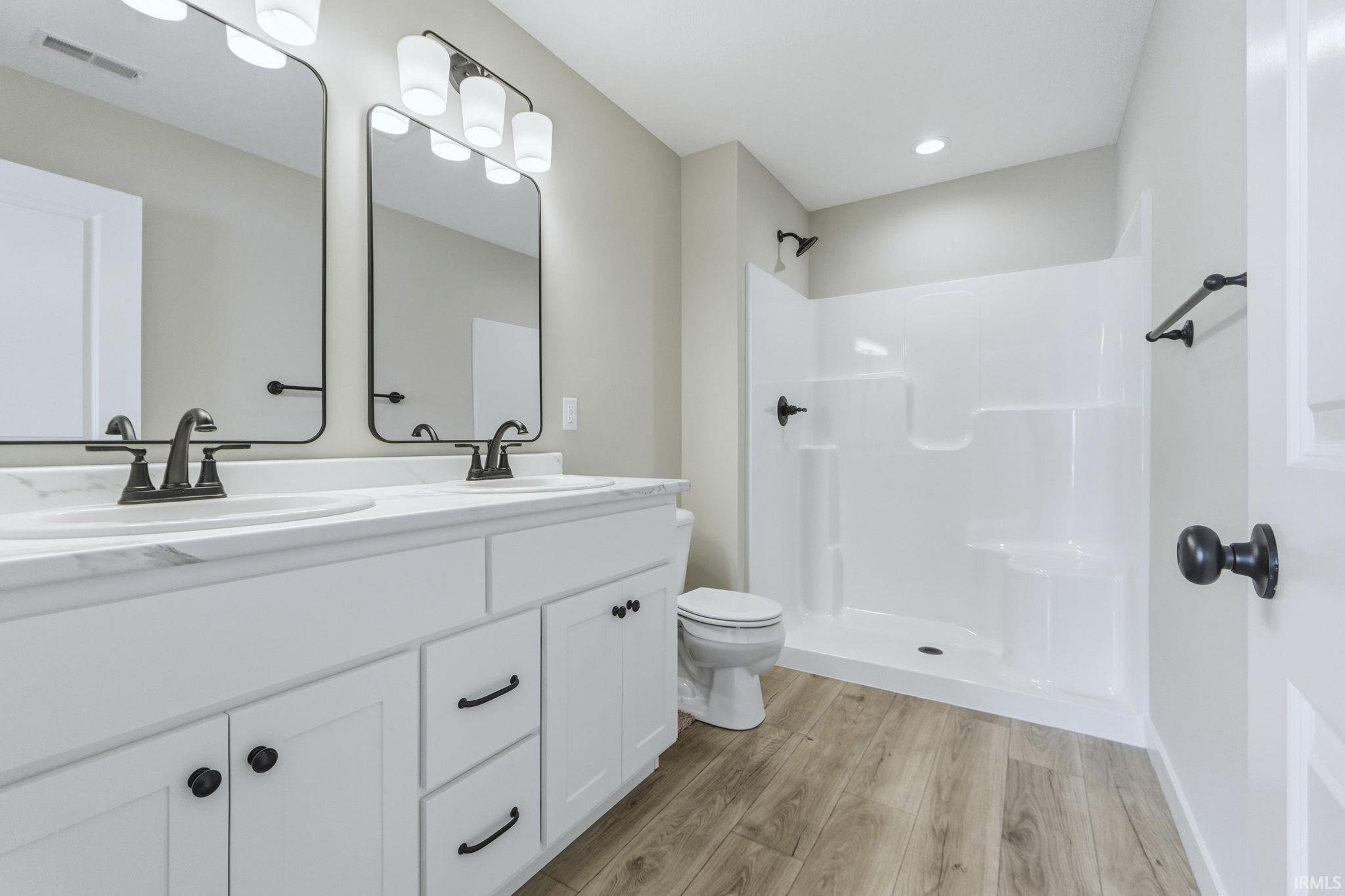 Bathroom featuring double vanity, light wood finished floors, and a shower