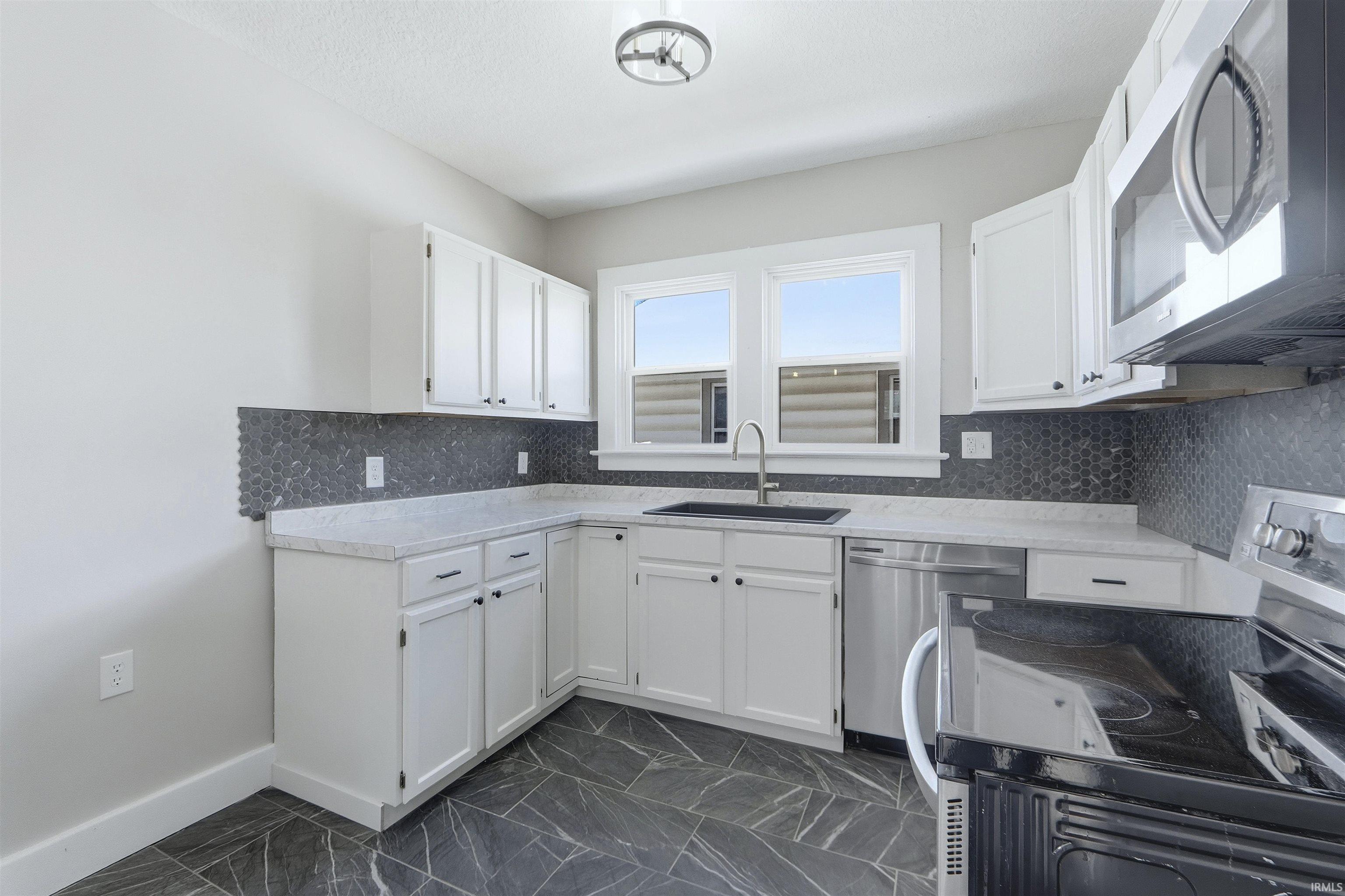 Kitchen with stainless steel appliances, white cabinetry, dark marble finish flooring, and backsplash