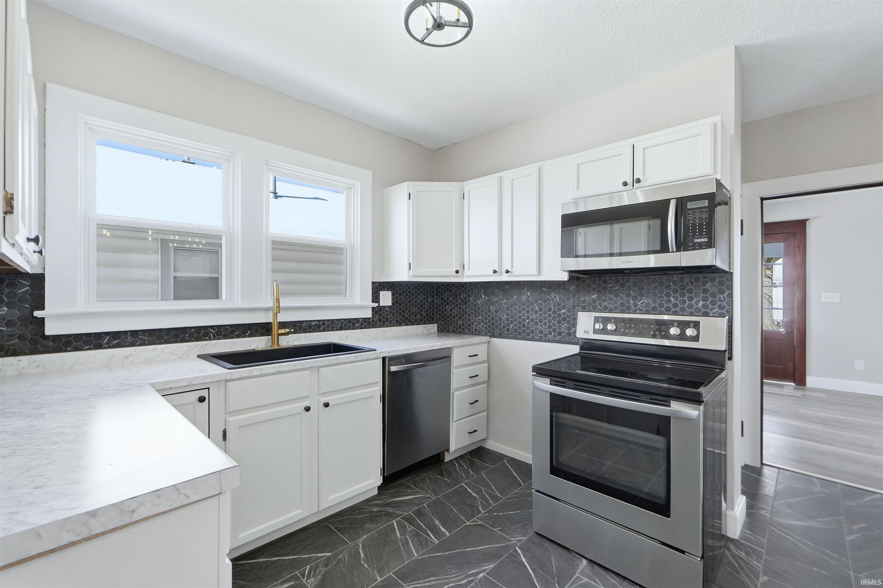 Kitchen with stainless steel appliances, light countertops, dark marble finish flooring, white cabinetry, and decorative backsplash
