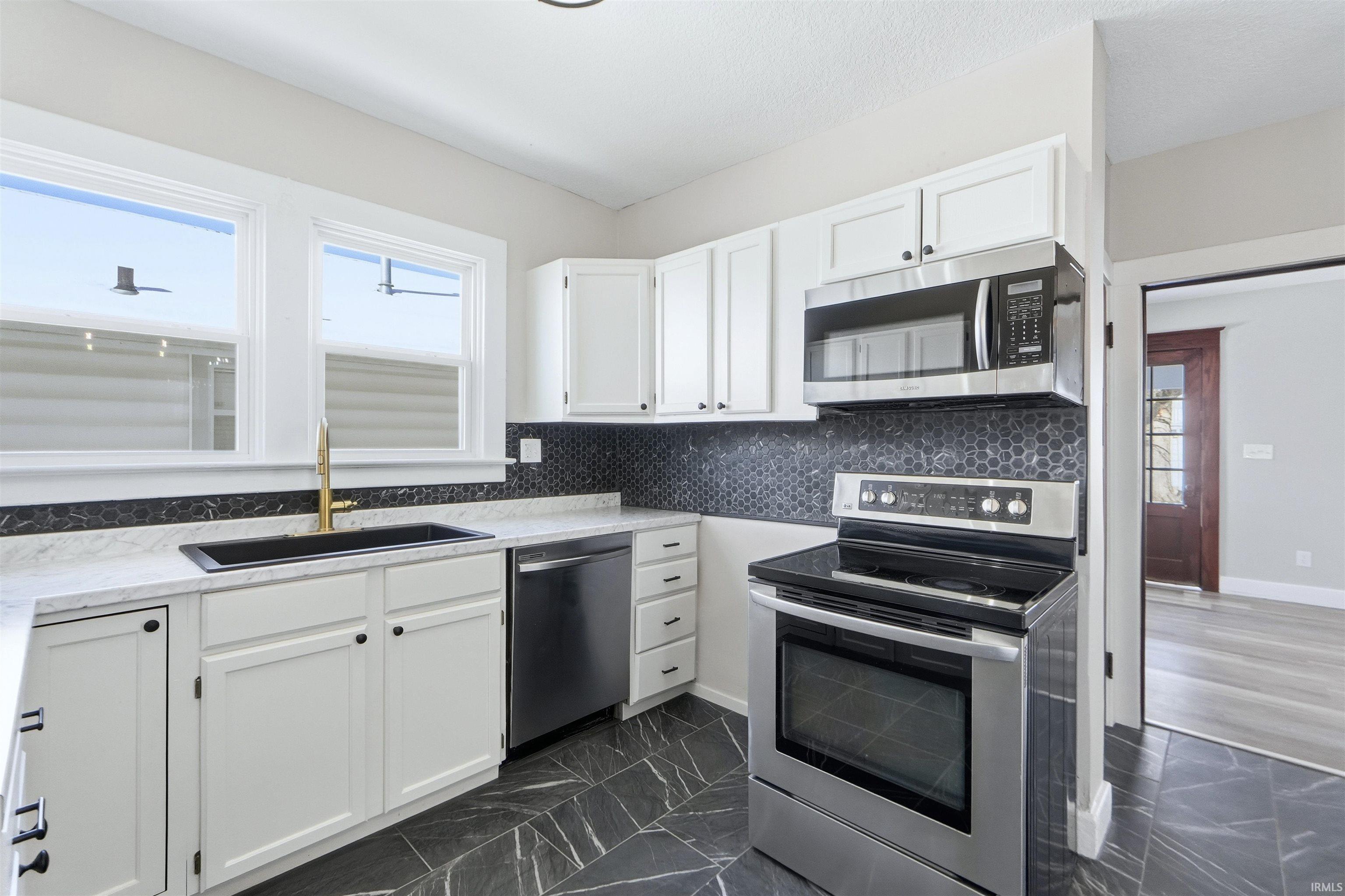Kitchen with appliances with stainless steel finishes, white cabinetry, dark marble finish flooring, and backsplash