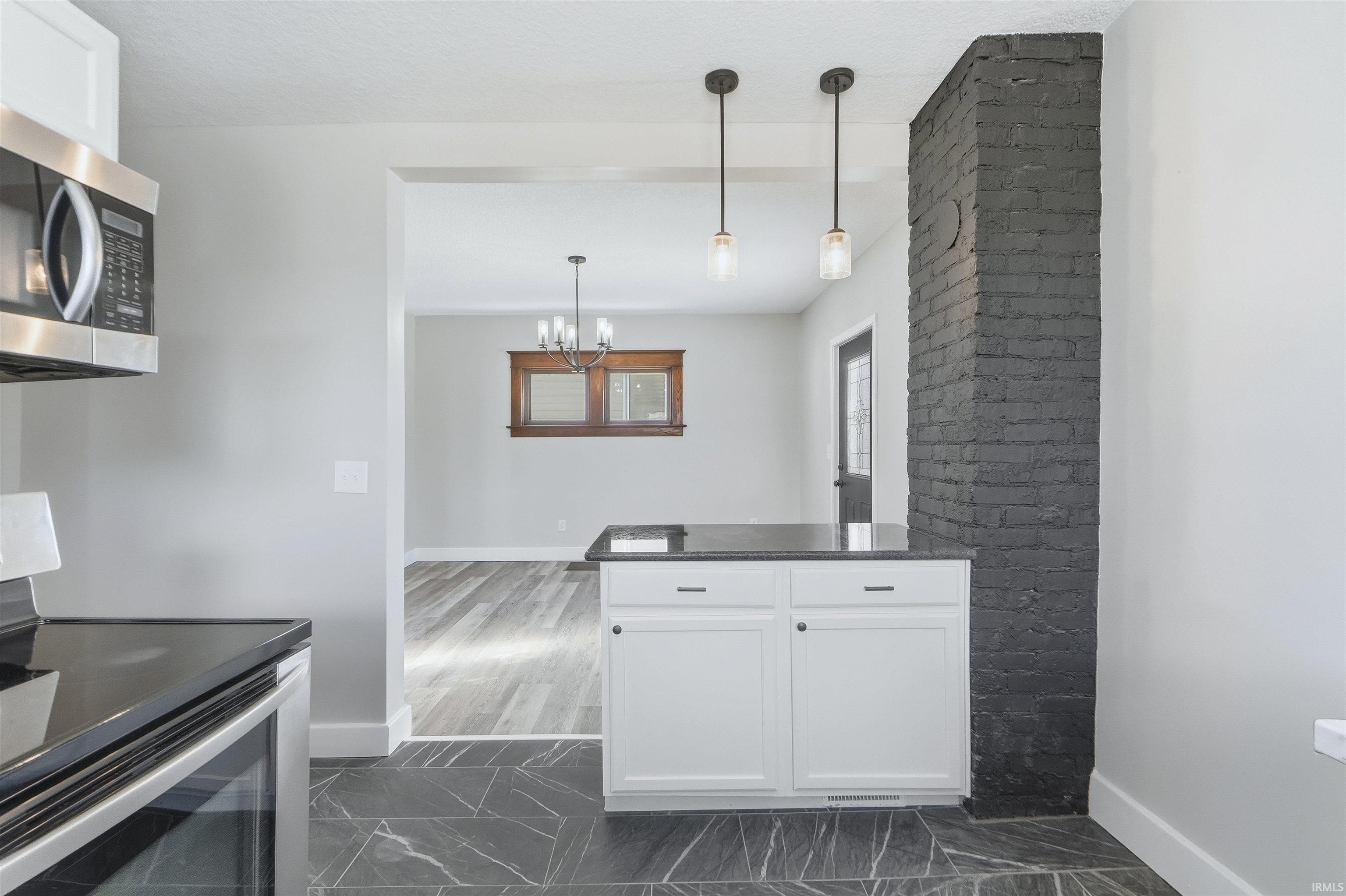 Kitchen with appliances with stainless steel finishes, white cabinetry, decorative light fixtures, and dark marble finish floors