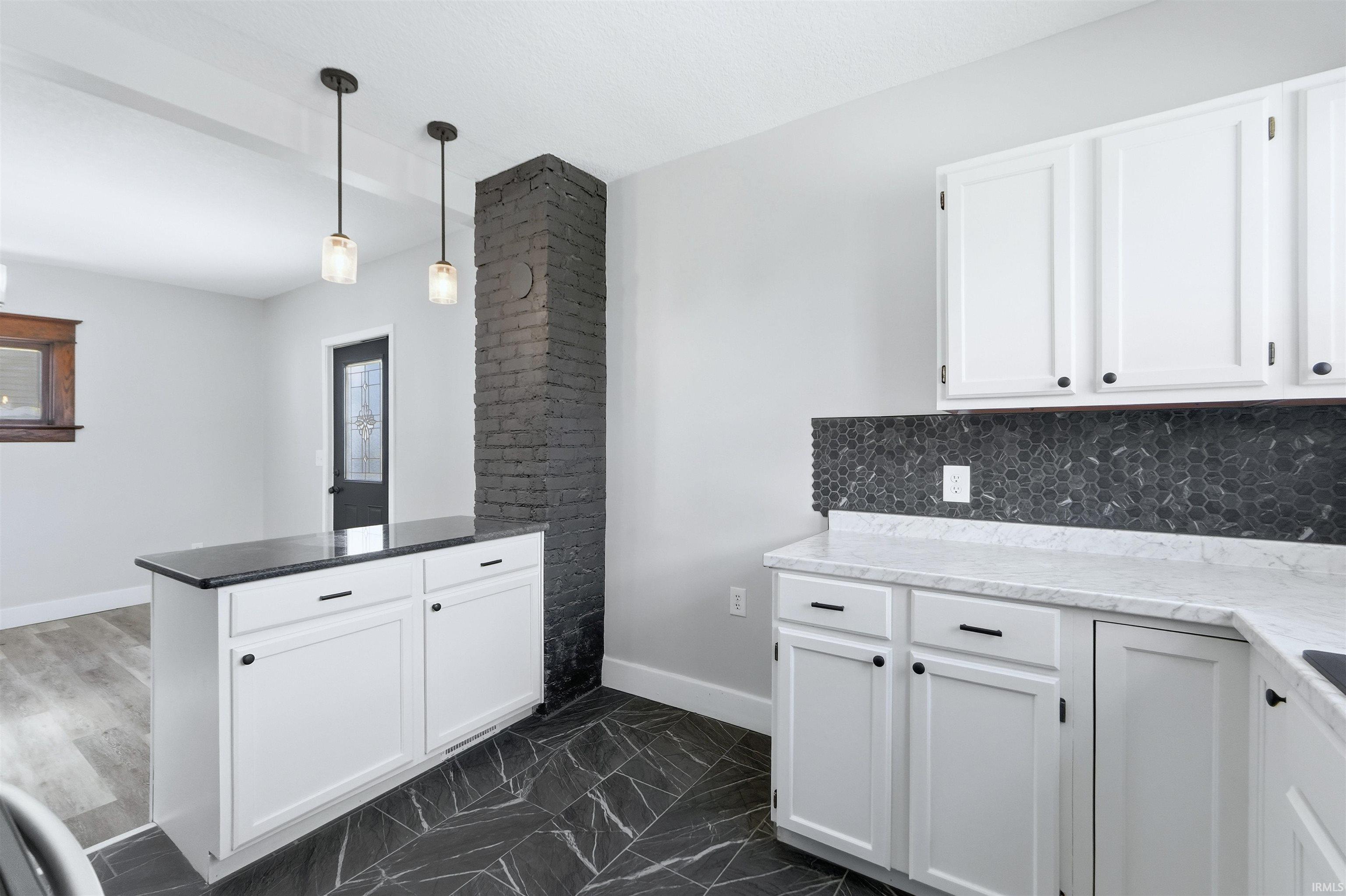 Kitchen featuring white cabinetry, pendant lighting, a peninsula, dark marble finish flooring, and decorative backsplash