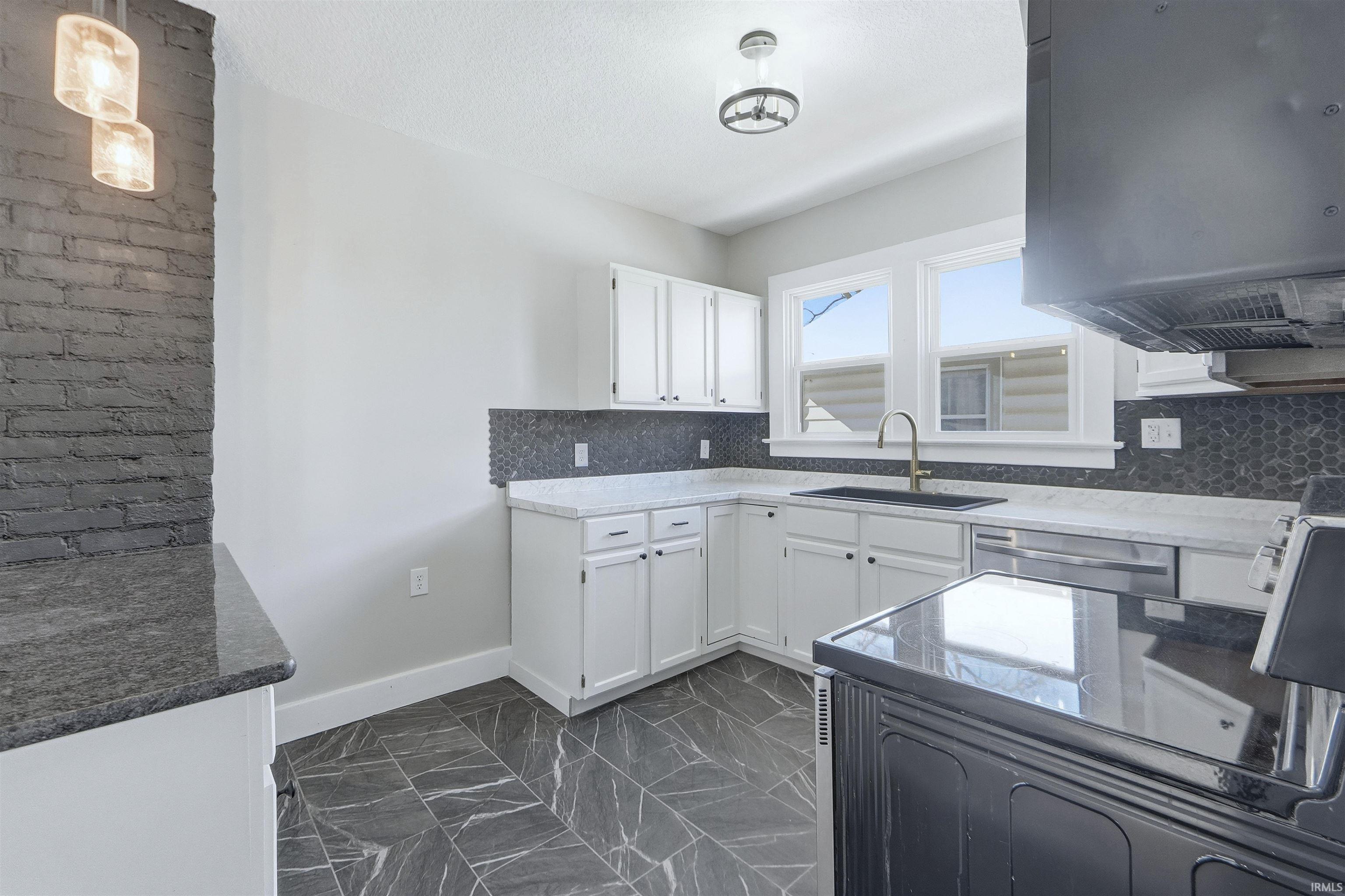 Kitchen with white cabinetry, dark marble finish floors, hanging light fixtures, range hood, and dishwasher