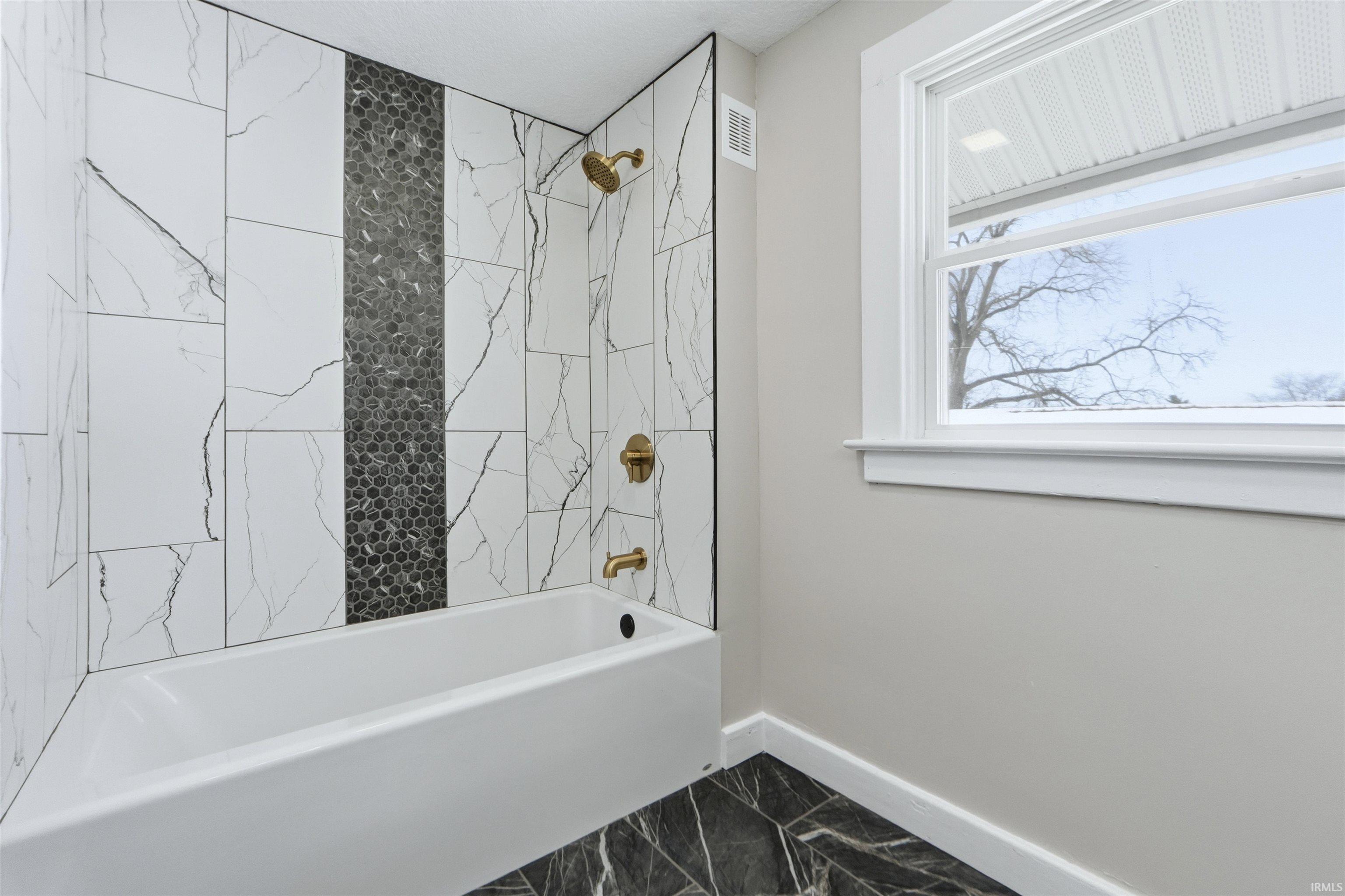 Bathroom featuring bathing tub / shower combination and dark marble finish floors