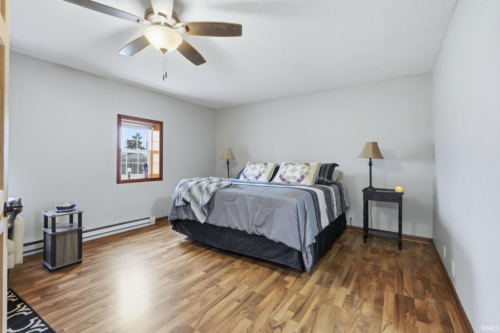 Bedroom featuring wood finished floors, baseboard heating, a ceiling fan, and a baseboard heating unit