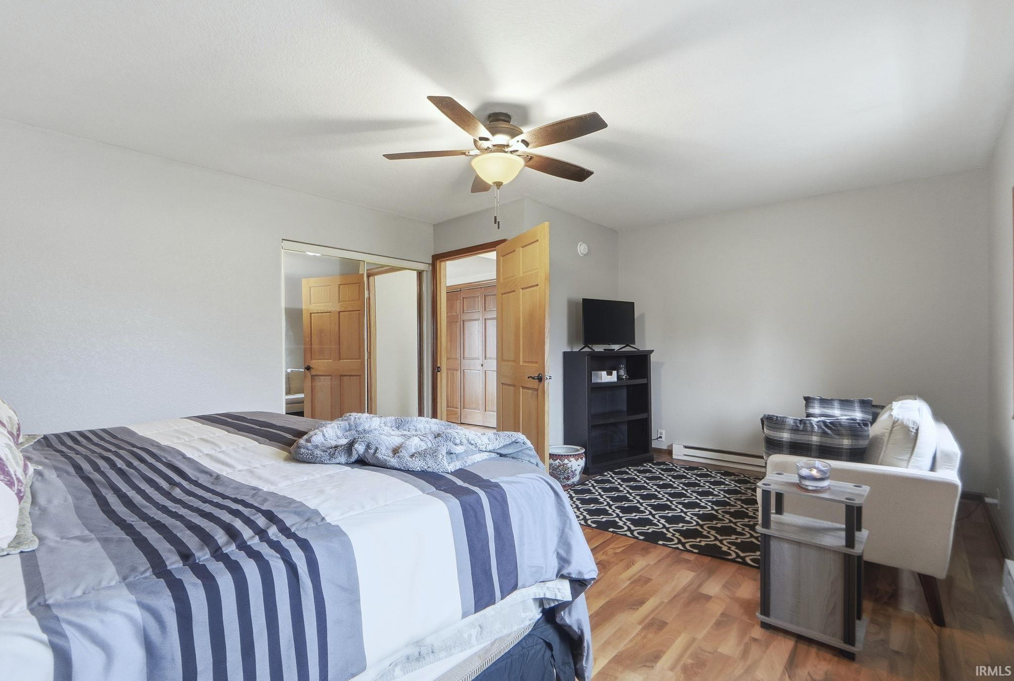 Bedroom with wood finished floors, baseboard heating, a closet, and ceiling fan