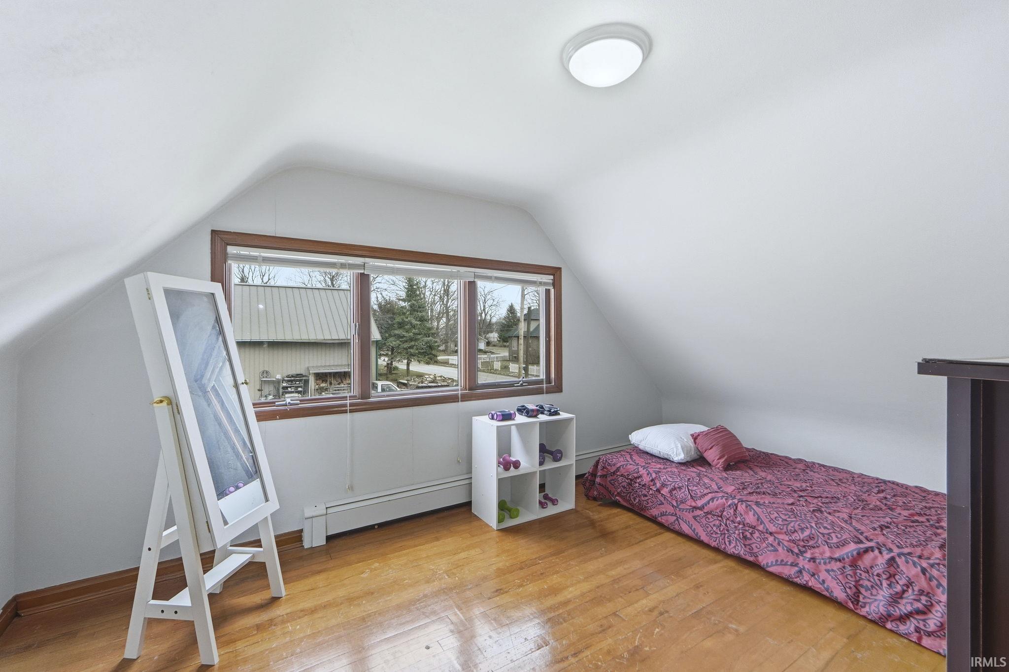 Bedroom featuring lofted ceiling, baseboard heating, and wood-type flooring