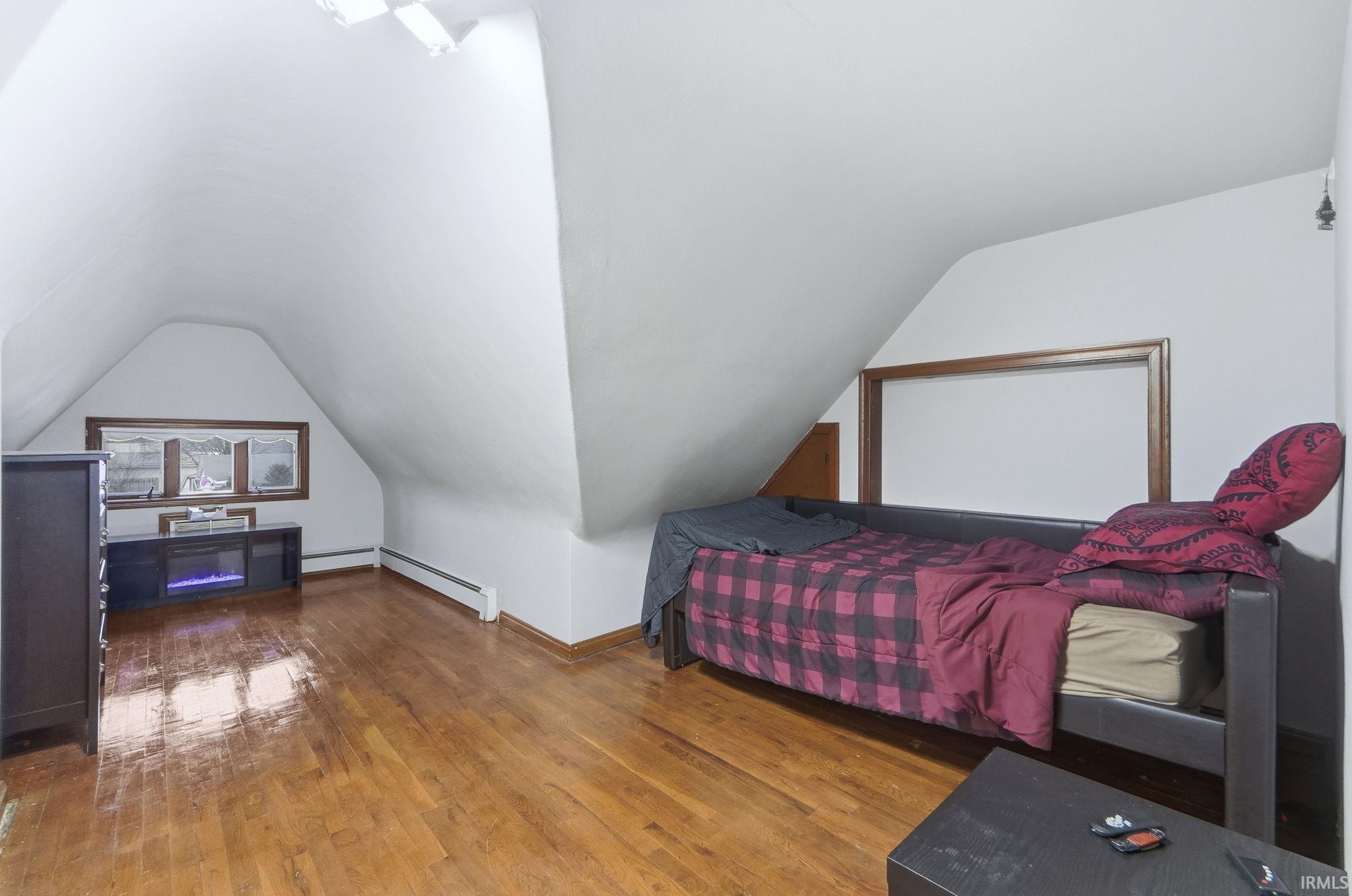 Bedroom featuring lofted ceiling, wood-type flooring, and a baseboard heating unit