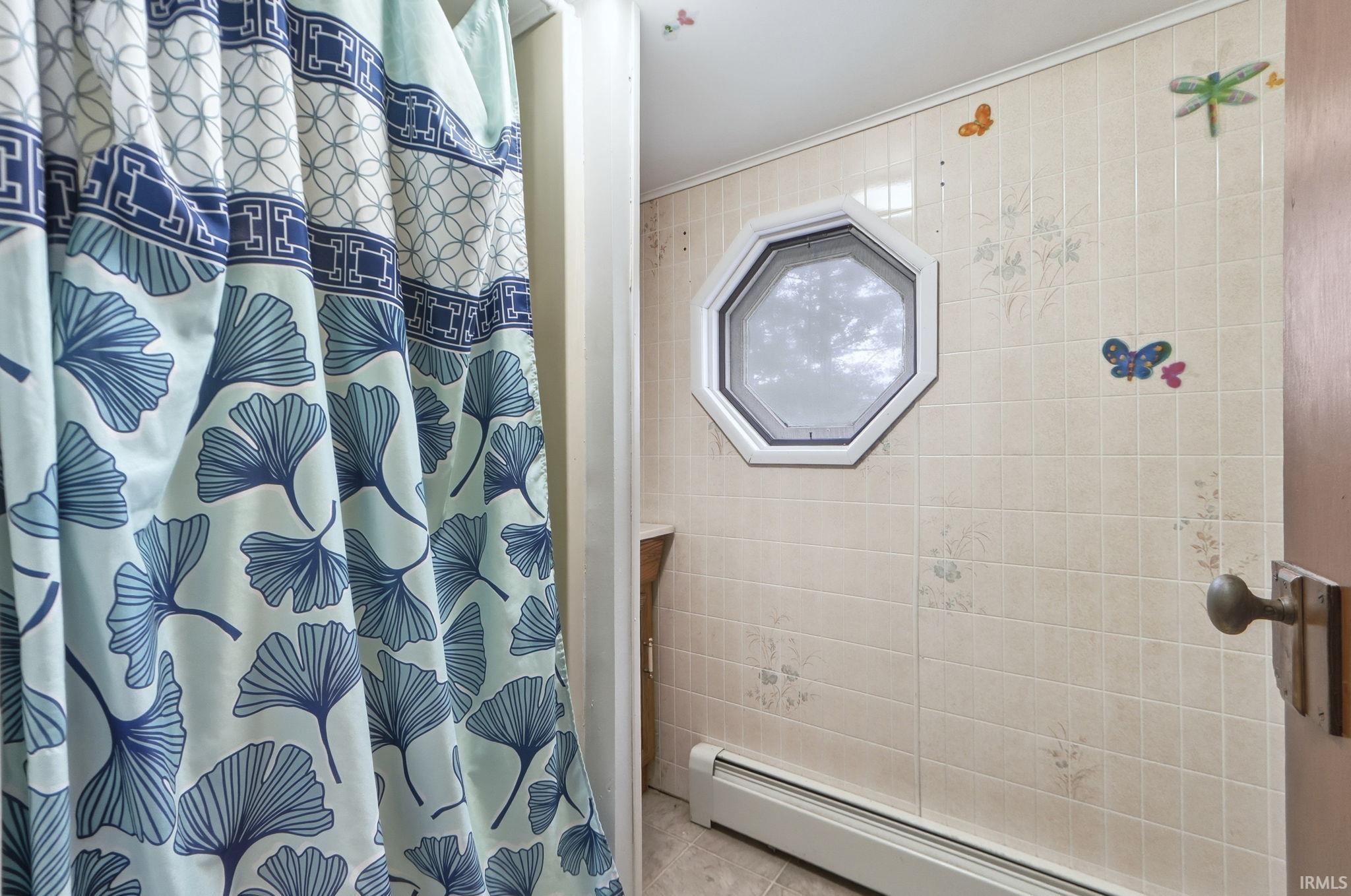 Bathroom with a baseboard radiator, a shower with shower curtain, crown molding, and tile patterned floors