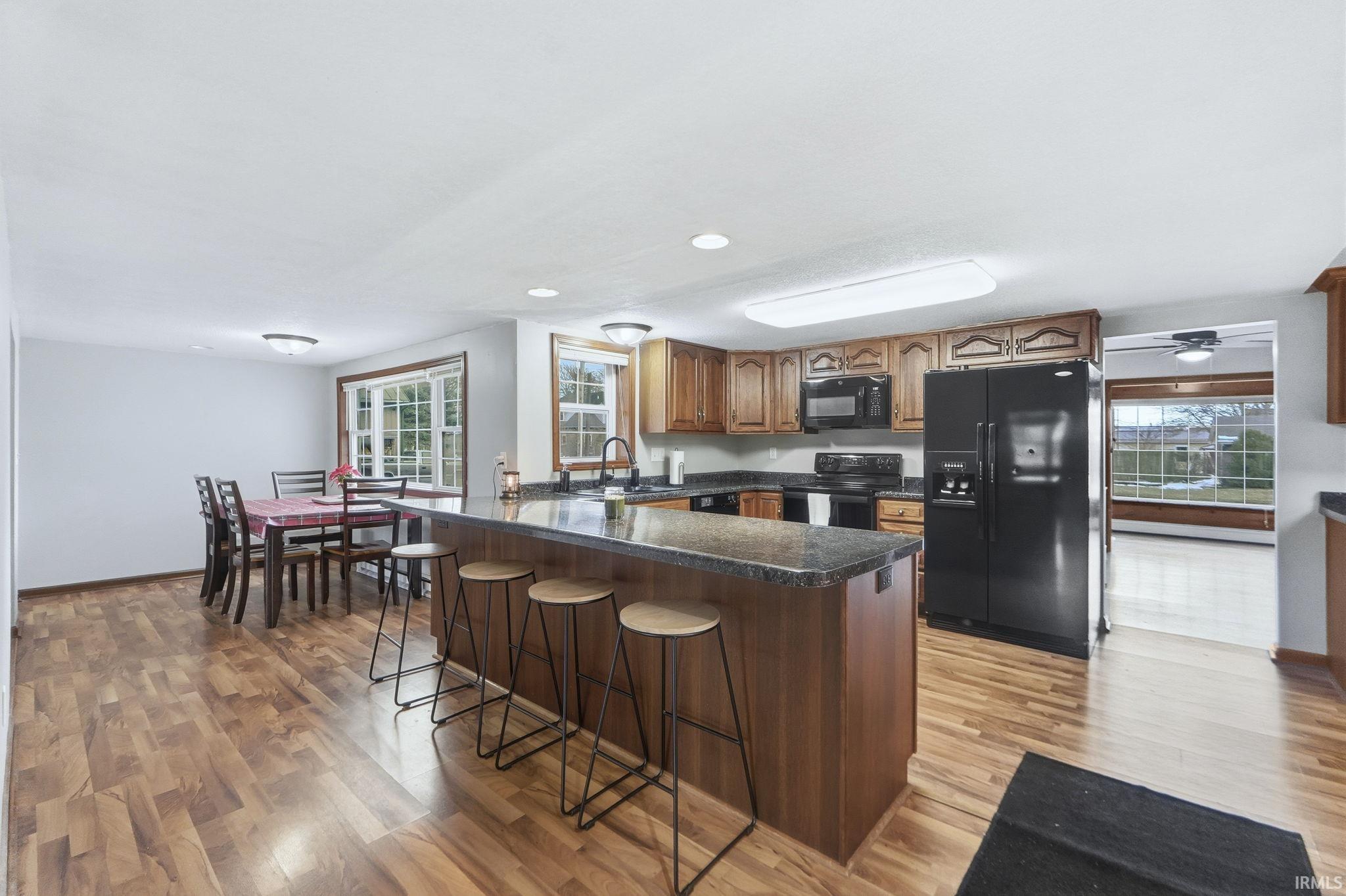 Kitchen featuring black appliances, a peninsula, brown cabinets, a kitchen bar, and light wood finished floors