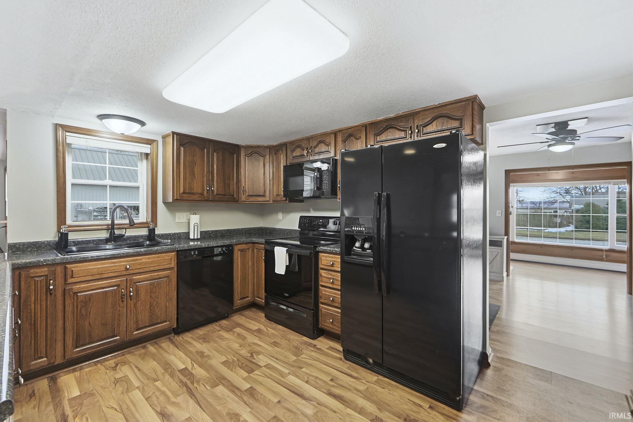 Kitchen with black appliances, light wood-type flooring, ceiling fan, a textured ceiling, and baseboard heating