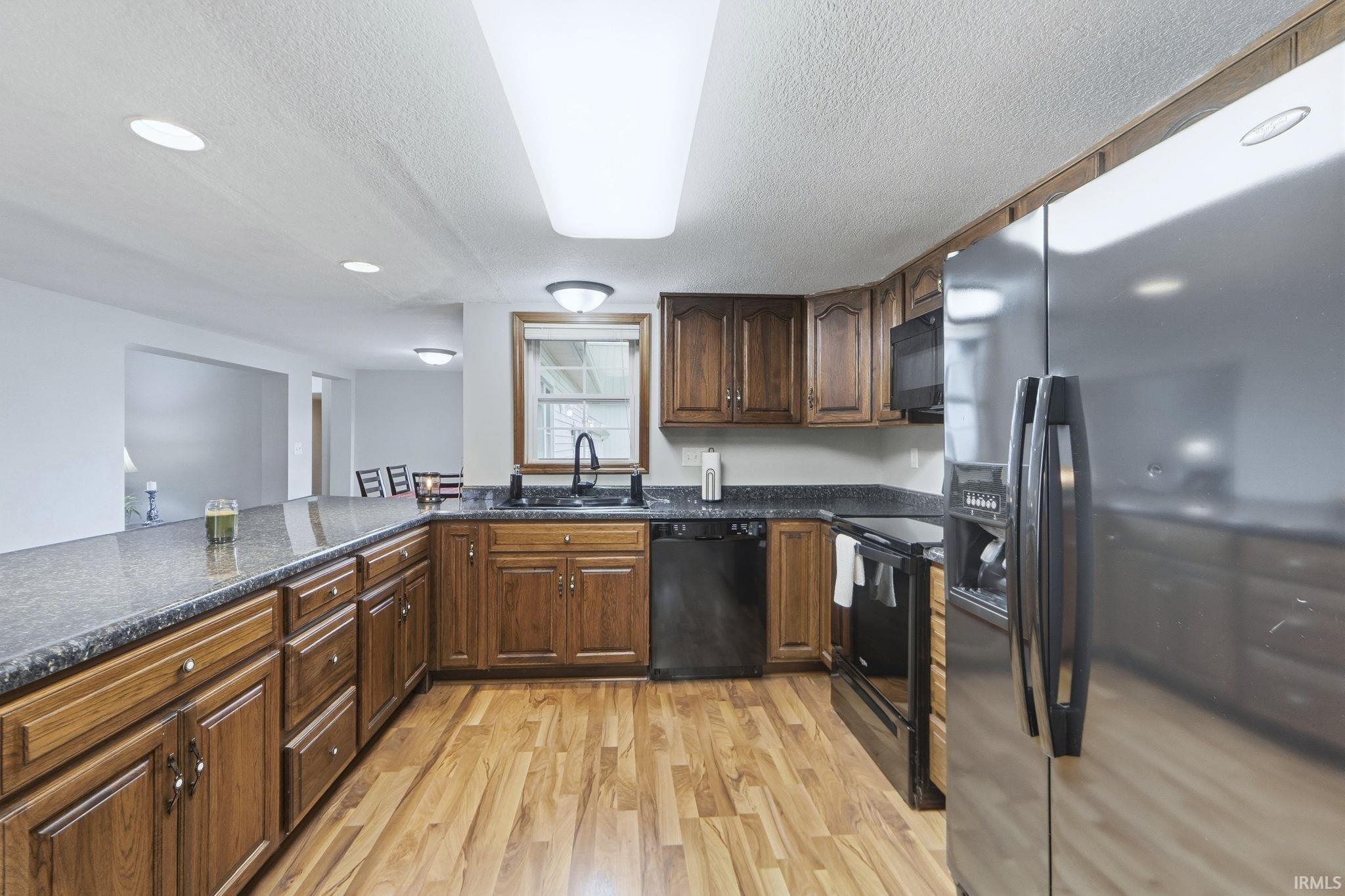 Kitchen featuring black appliances, a textured ceiling, light wood-type flooring, dark stone counters, and dark brown cabinets