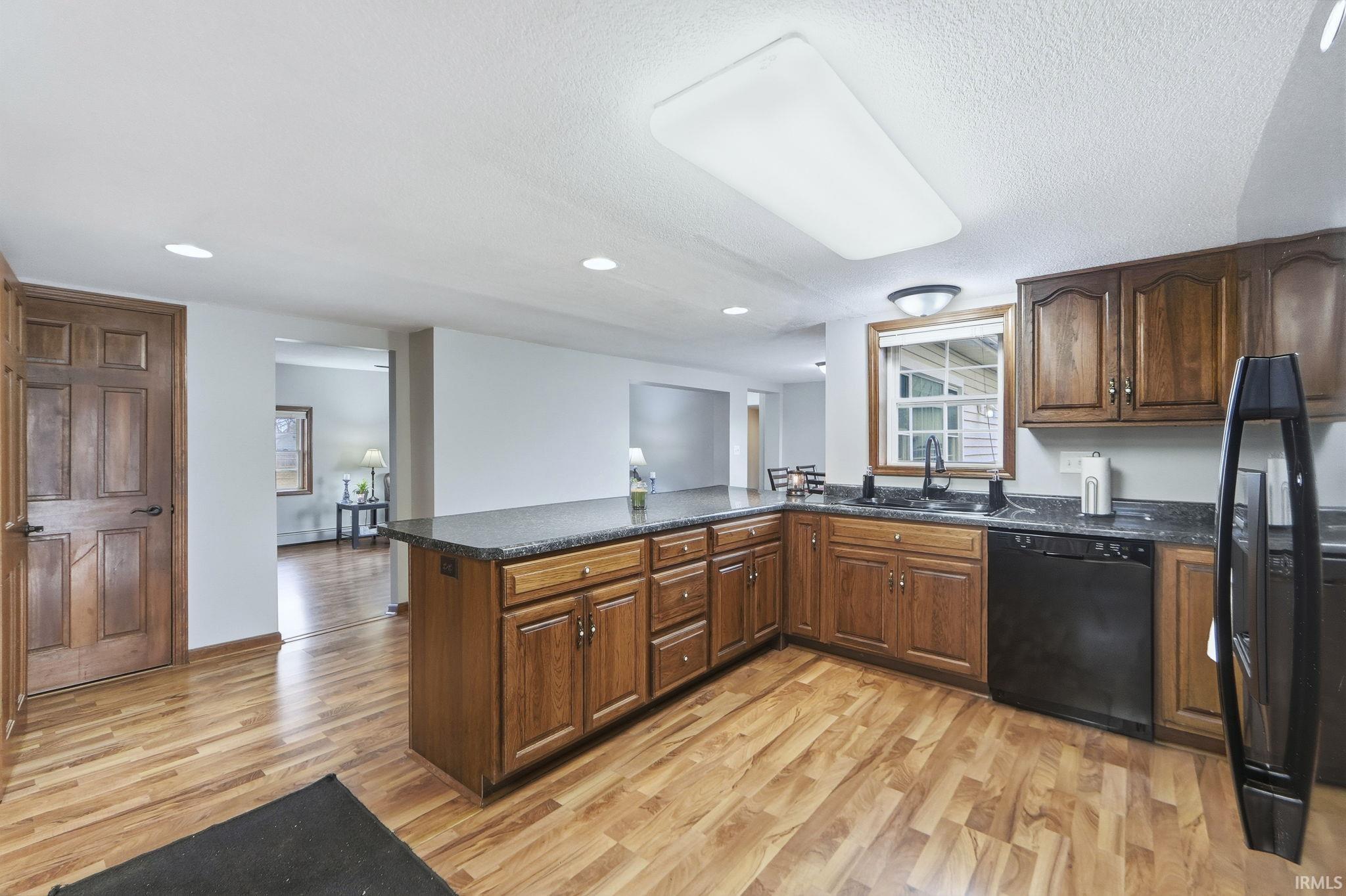 Kitchen with a peninsula, black appliances, light wood-style floors, and dark brown cabinetry
