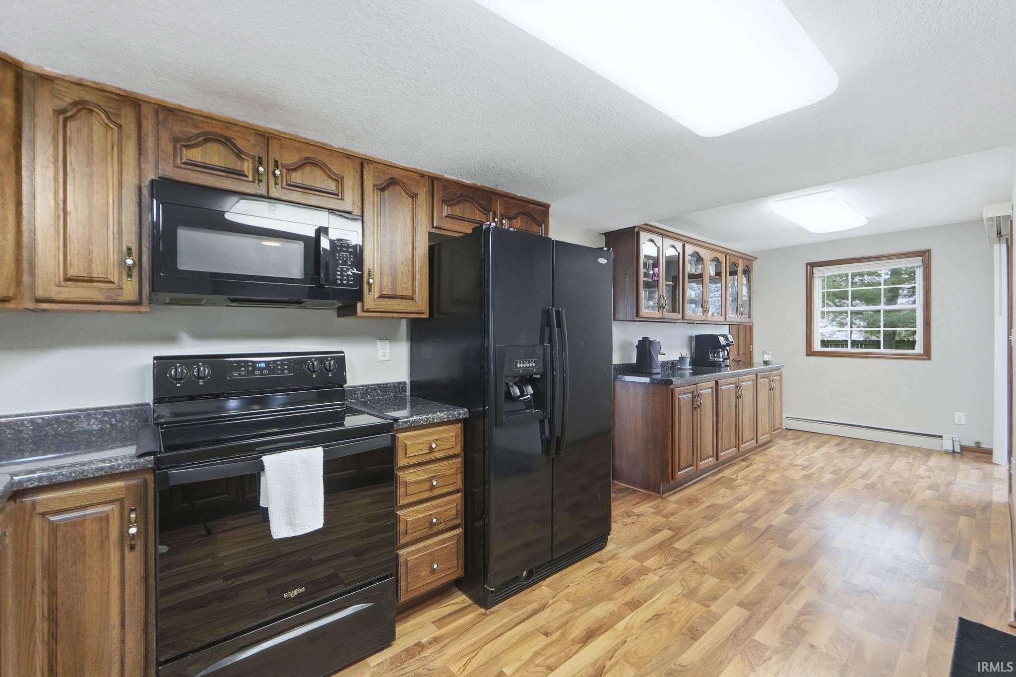 Kitchen with black appliances, brown cabinetry, glass insert cabinets, and a textured ceiling