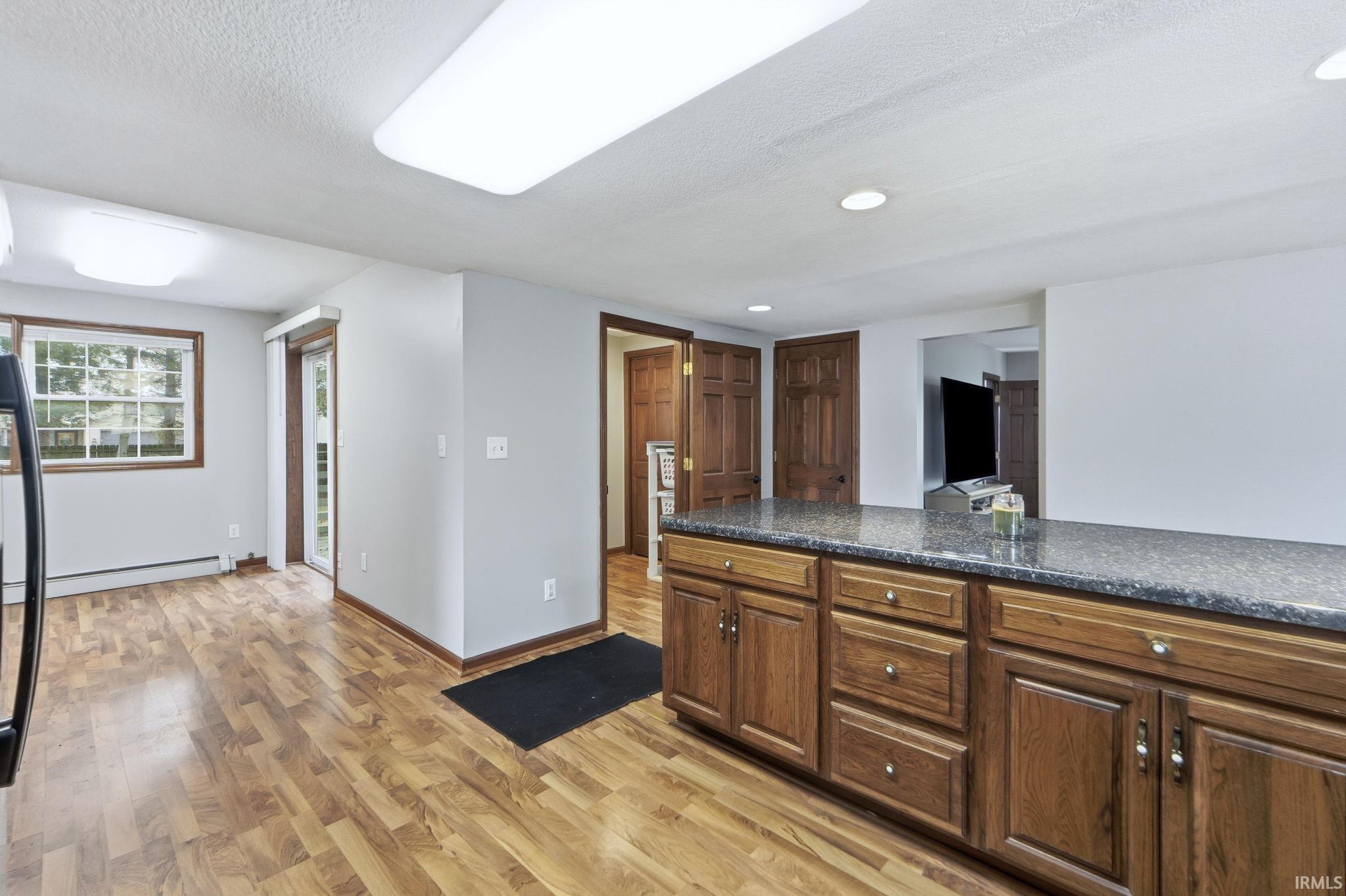 Kitchen with light wood-type flooring, a textured ceiling, a baseboard heating unit, recessed lighting, and brown cabinetry