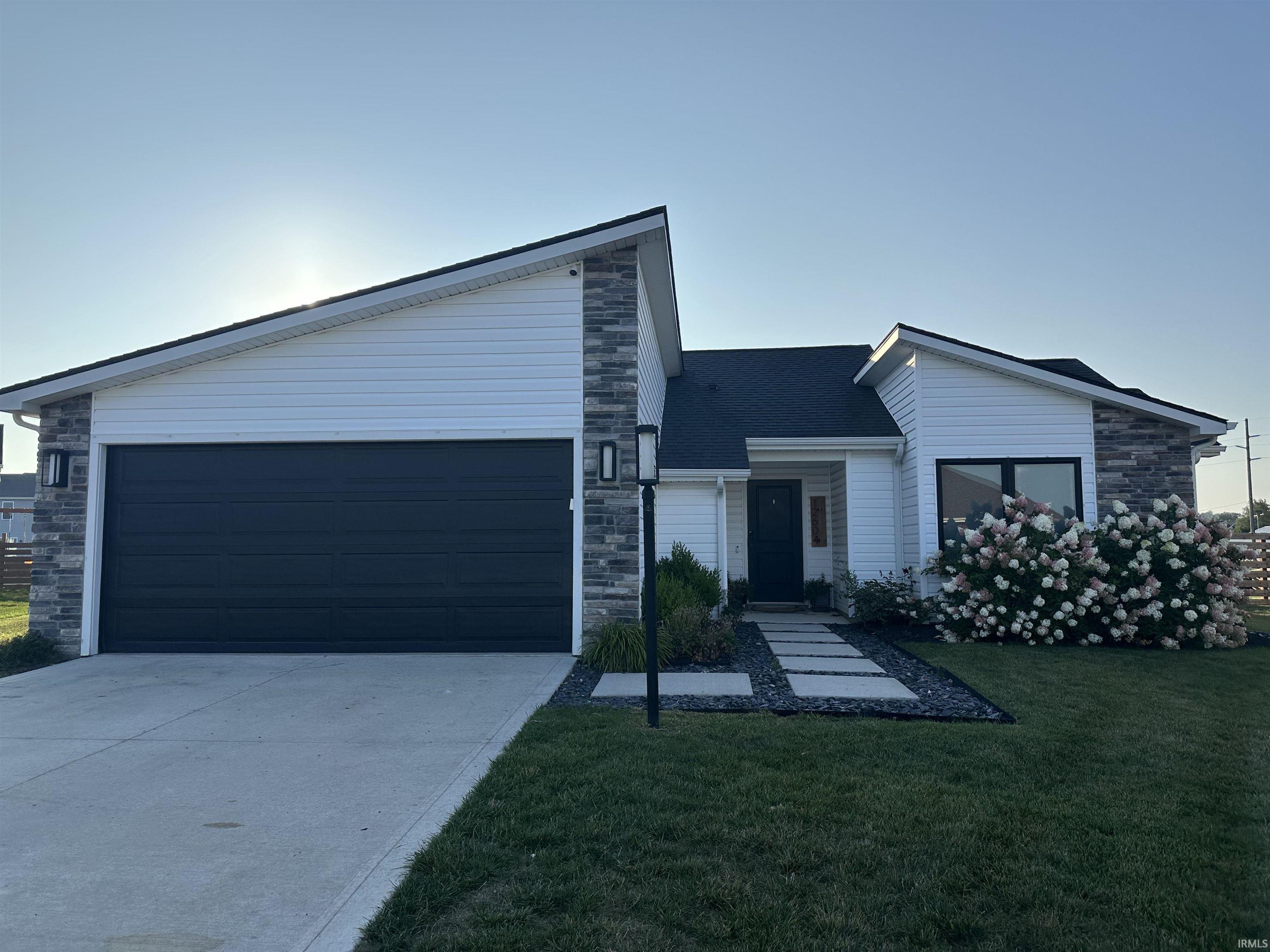Mid-century home with stone siding, concrete driveway, a front yard, and an attached garage